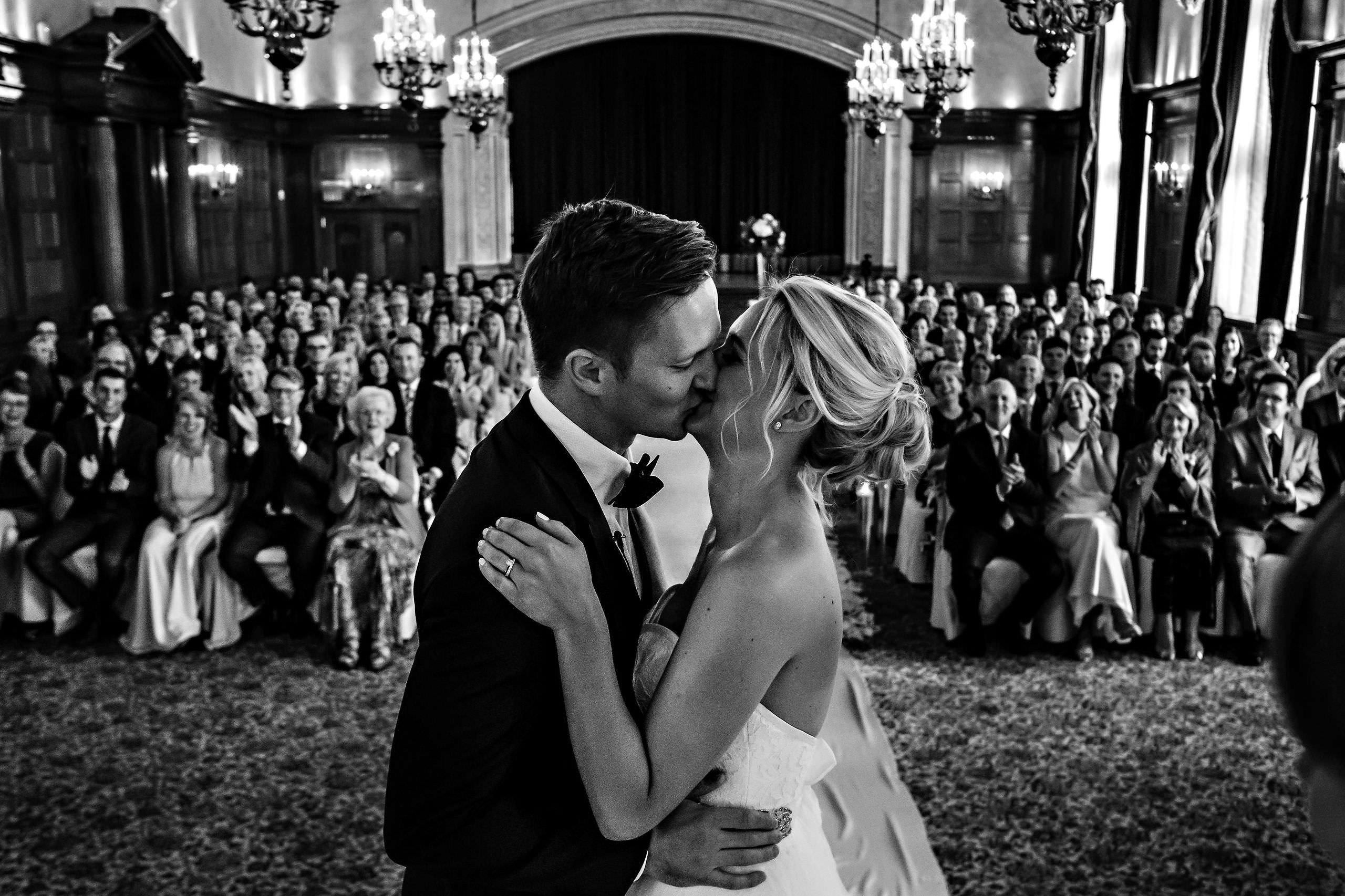 Winnipeg wedding photography captures a couple kissing in front of guests in a grand hall.