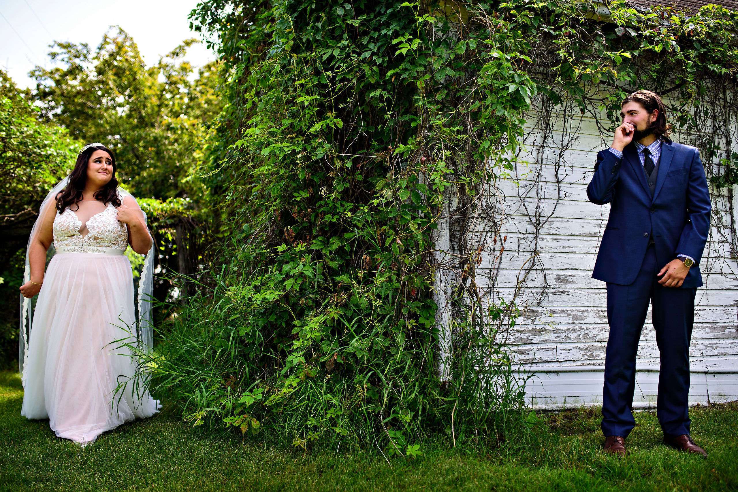 Bride and groom stand apart by vine-covered wall, captured by Winnipeg wedding photography.