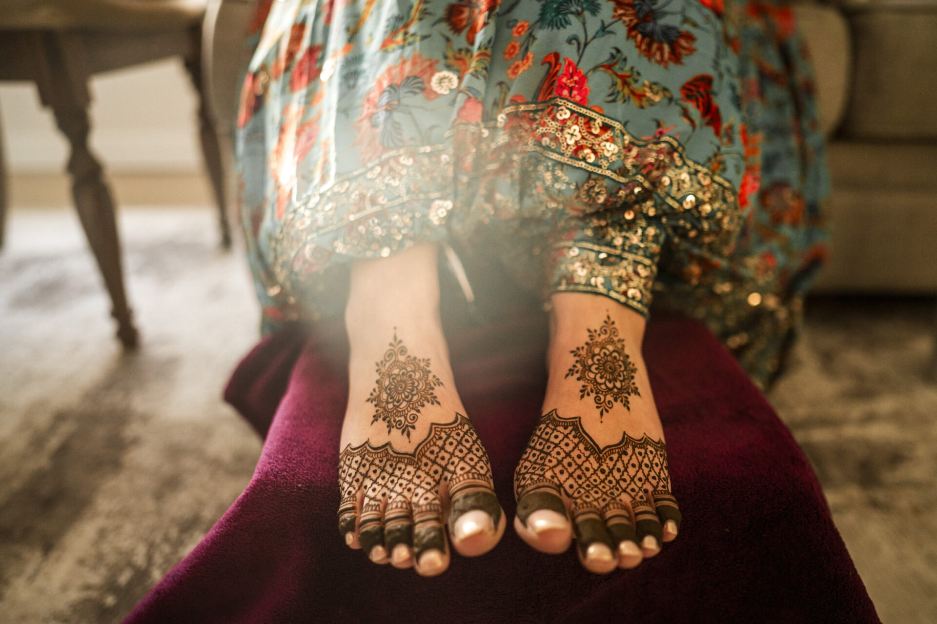 Feet adorned with intricate henna, under a colorful garment at a vibrant Hindu wedding.