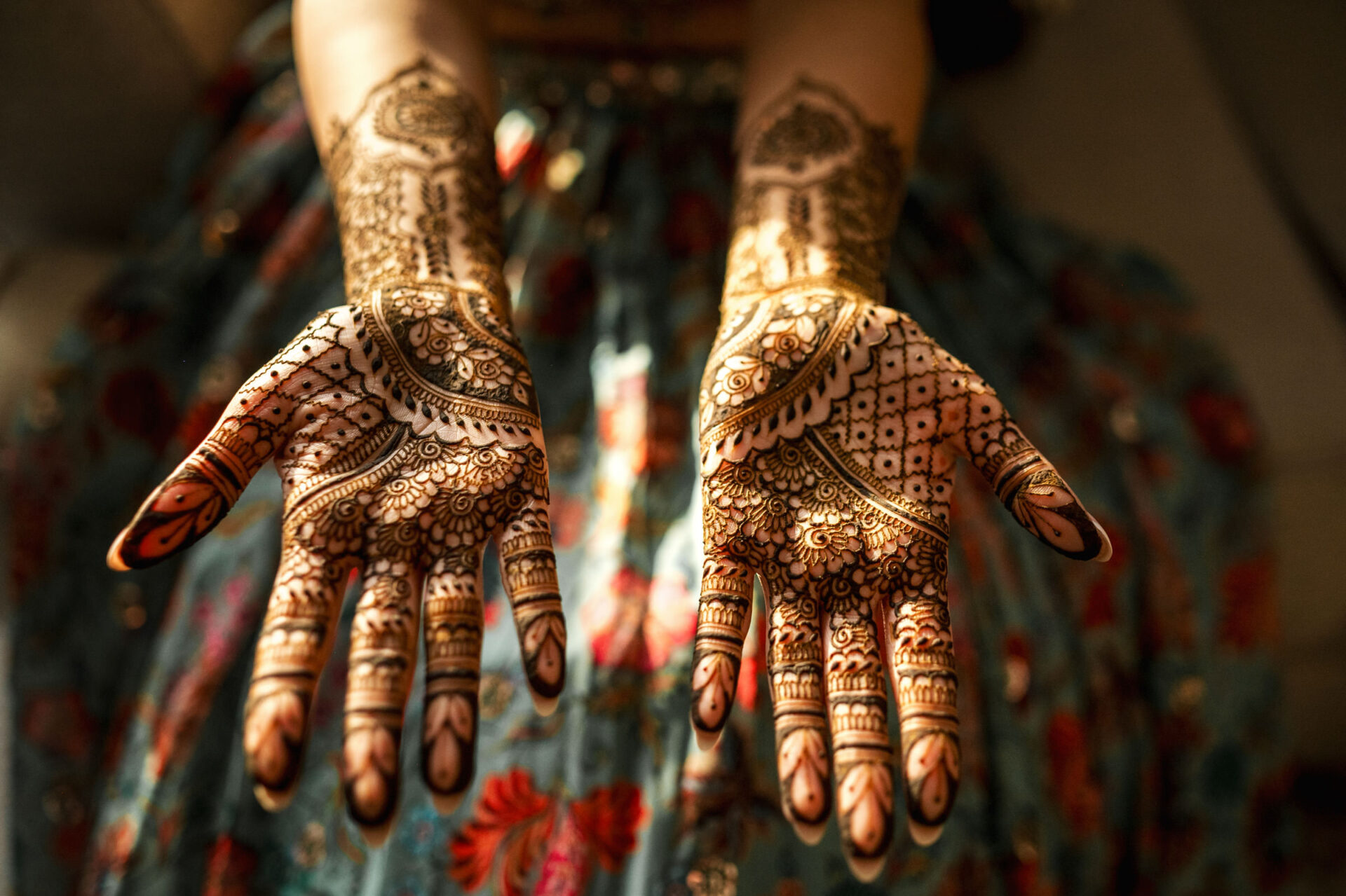 Hands with intricate henna designs, palms up, on a vibrant Sikh wedding backdrop.