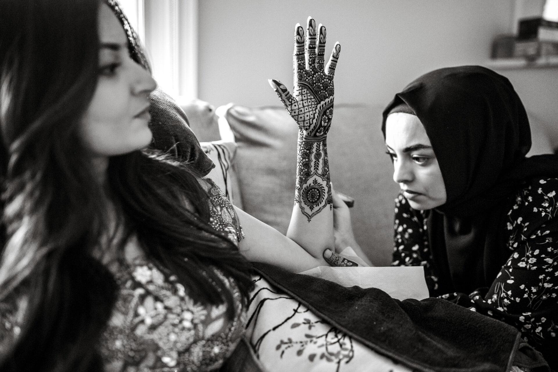 At a Sikh wedding, a woman adorns another's arm with intricate henna designs.