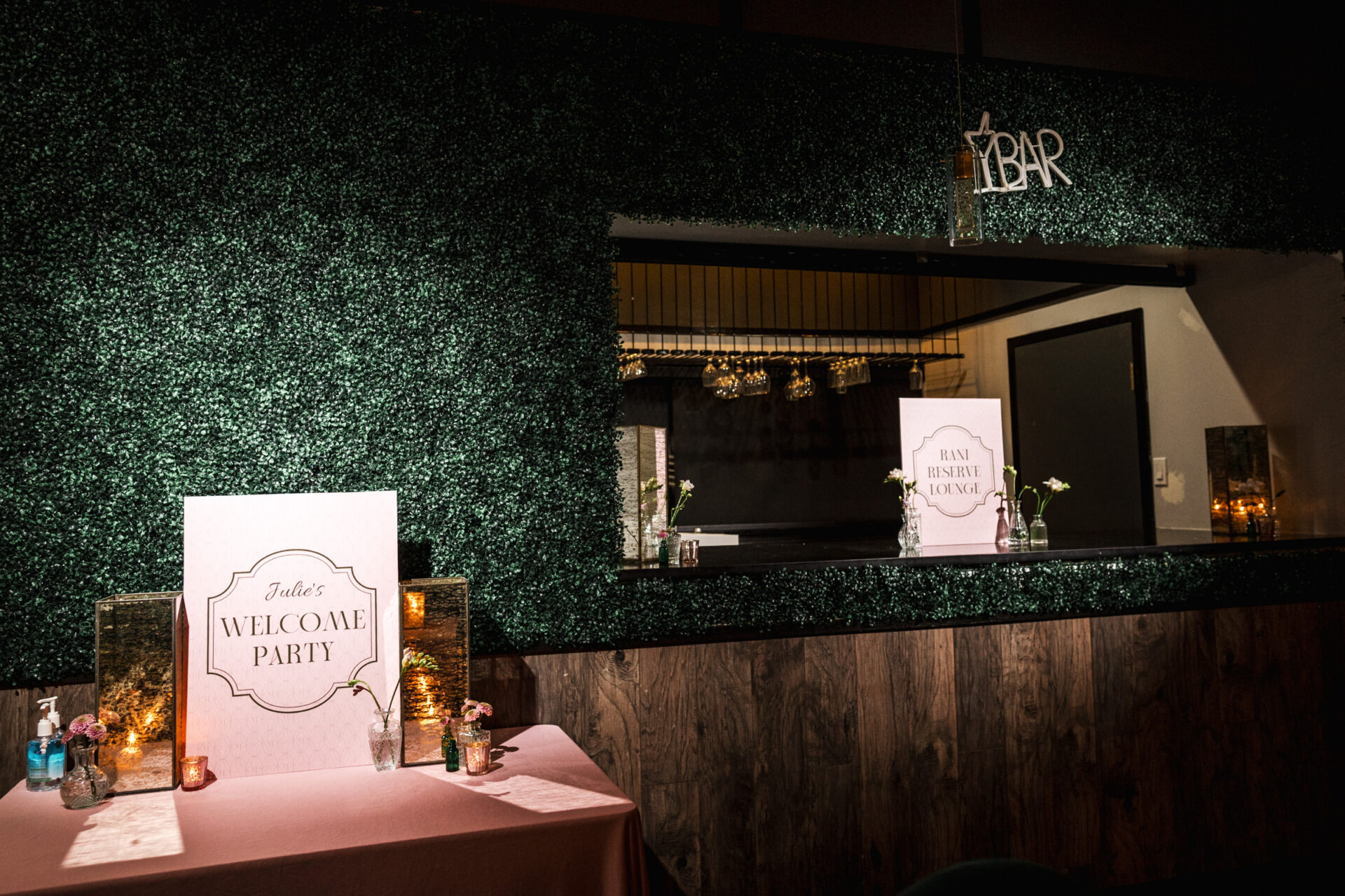 Sikh & Hindu wedding indoor setup with a greenery wall and "Welcome Party" sign near a T-bar.