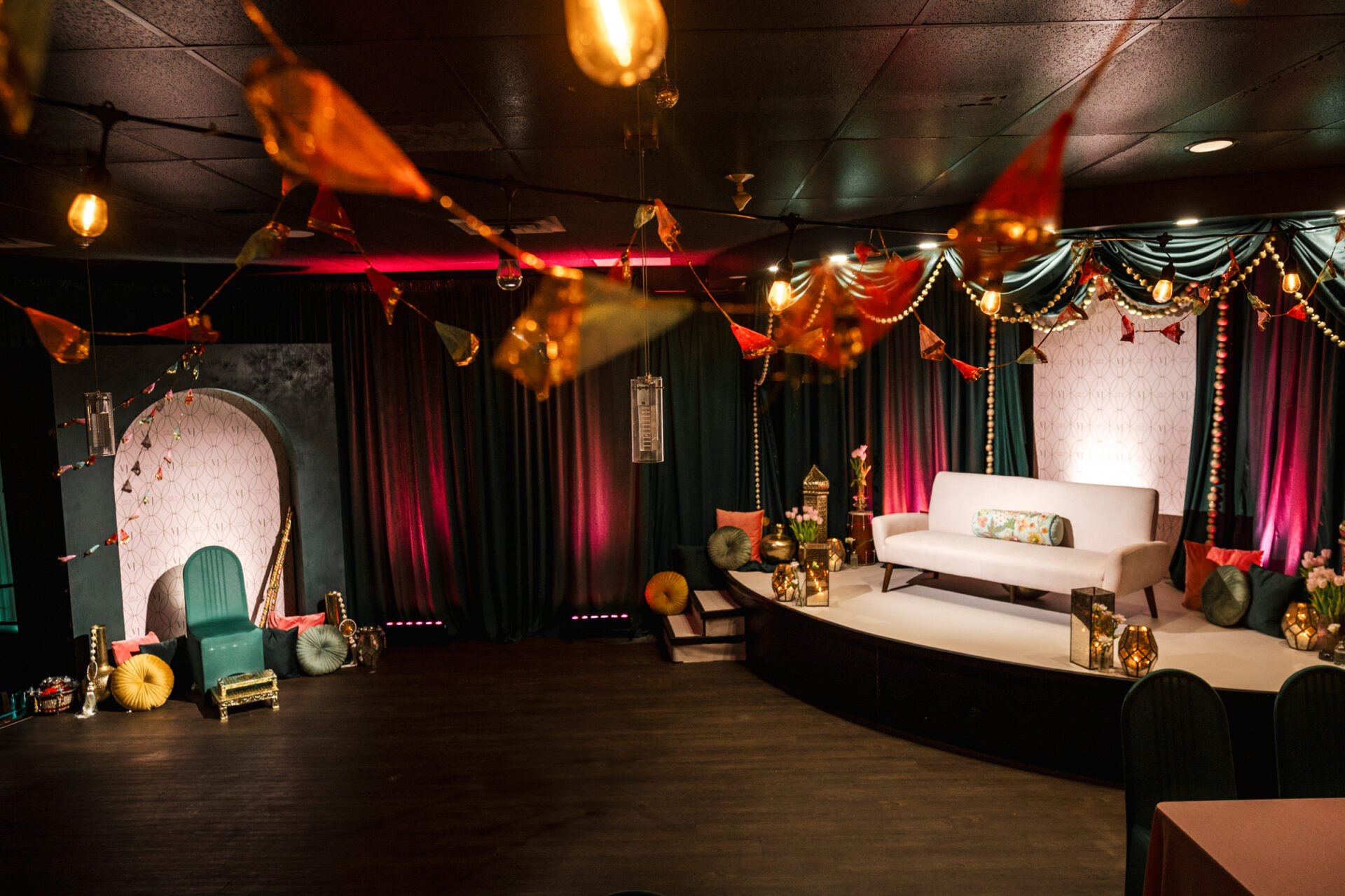 Decorative room with stage, sofa, colorful cushions, and string lights for a Sikh wedding.