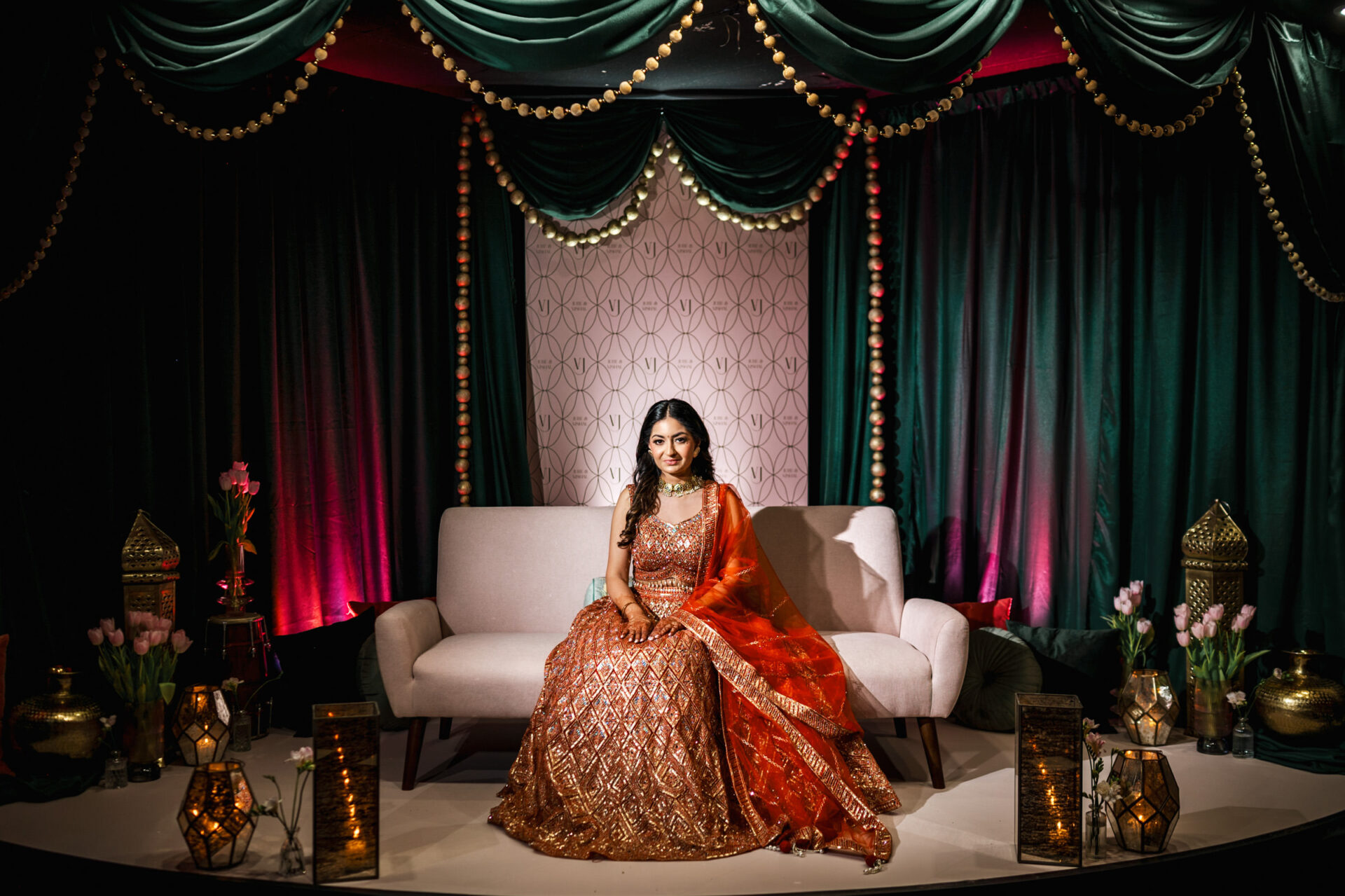 Woman in ornate dress, surrounded by lanterns and draped fabric, at a Sikh wedding.