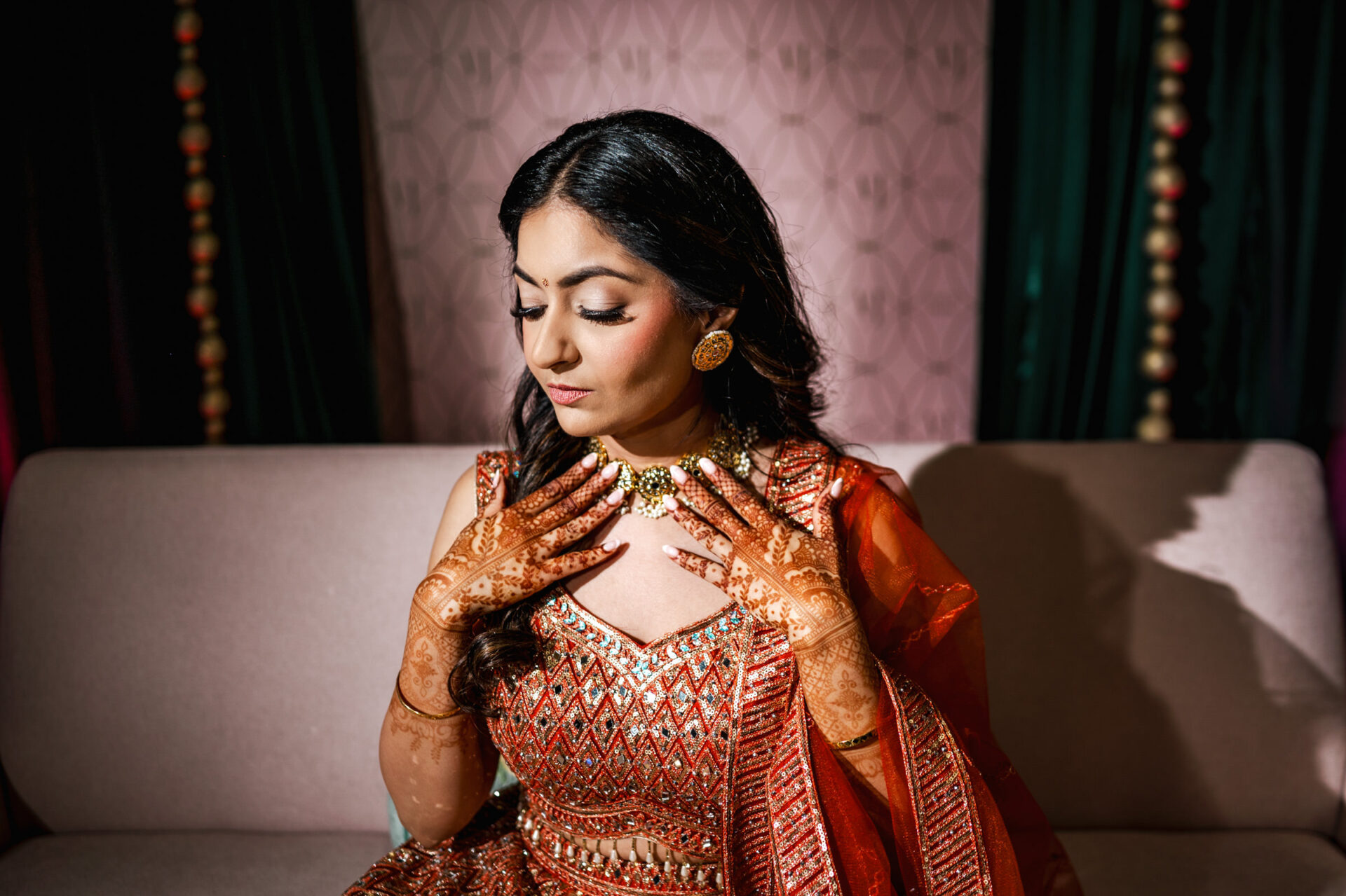 Woman in ornate red attire at a Sikh wedding, showing henna on hands, against a patterned backdrop.