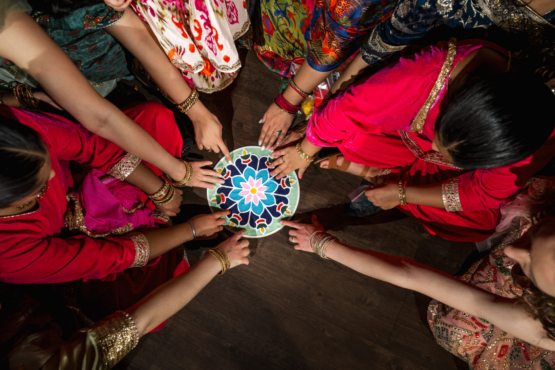 Women in traditional clothing craft a colorful rangoli for a vibrant Hindu wedding.