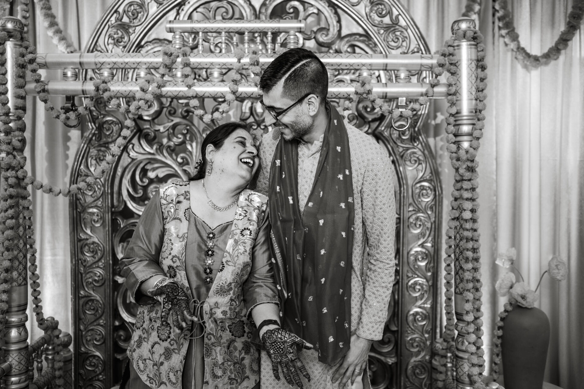 A couple joyfully laughing in traditional attire at a vibrant Sikh wedding.