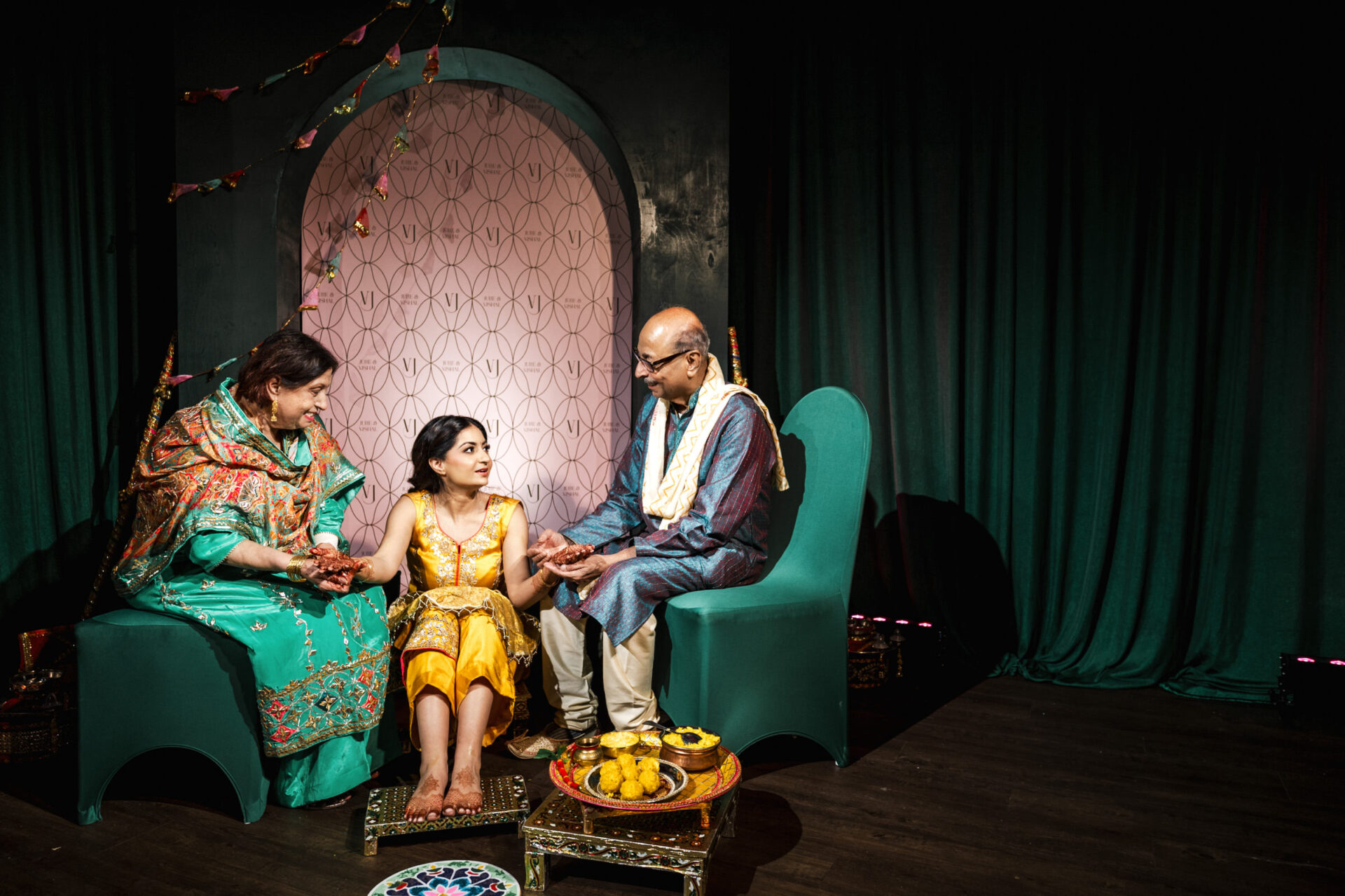 A woman in a yellow dress sits with two people in traditional attire at a Hindu wedding.