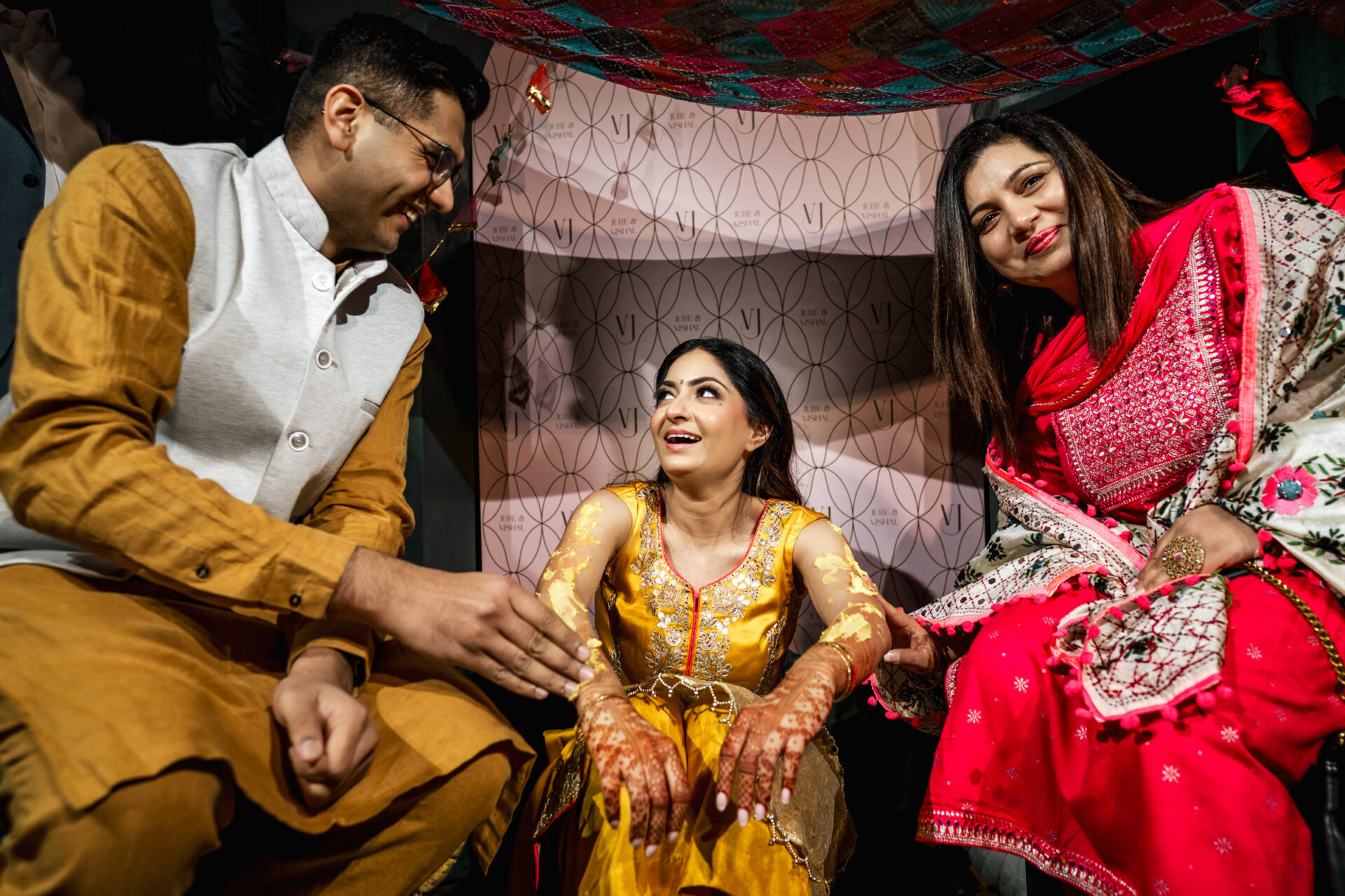 Three people in vibrant attire and henna, celebrating a Sikh wedding under a decorative canopy.