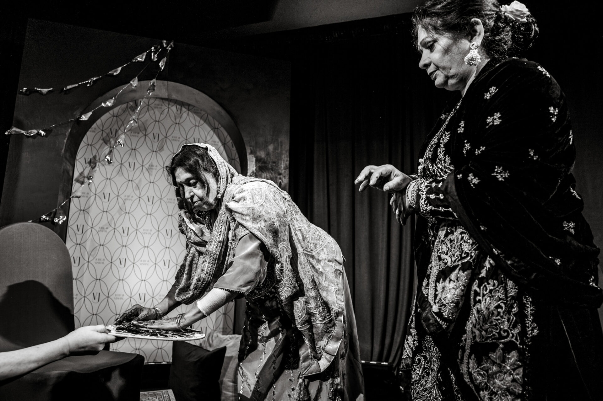 Two women in traditional attire, like a Sikh or Hindu wedding scene, engage with an unseen person.