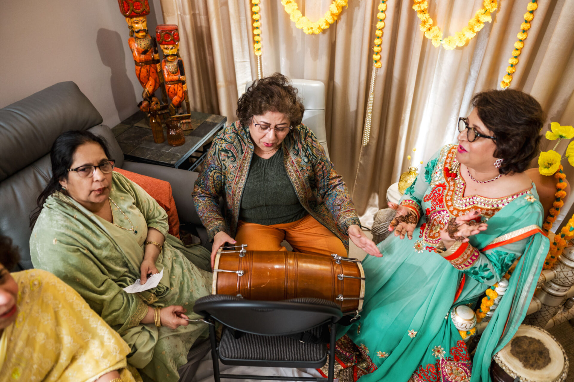 Four women in colorful attire at a festive Sikh wedding, one playing a drum.