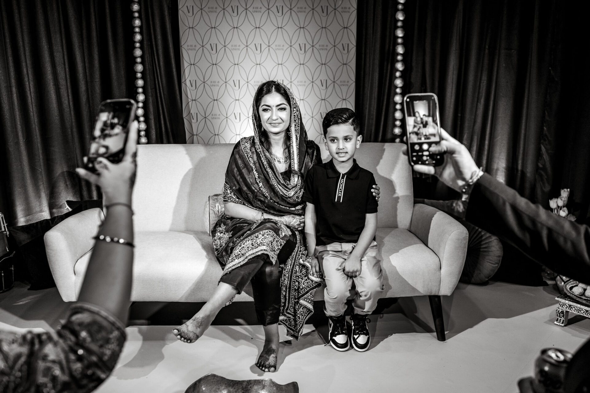A woman and boy pose on a couch at a lively Sikh wedding as others snap photos.