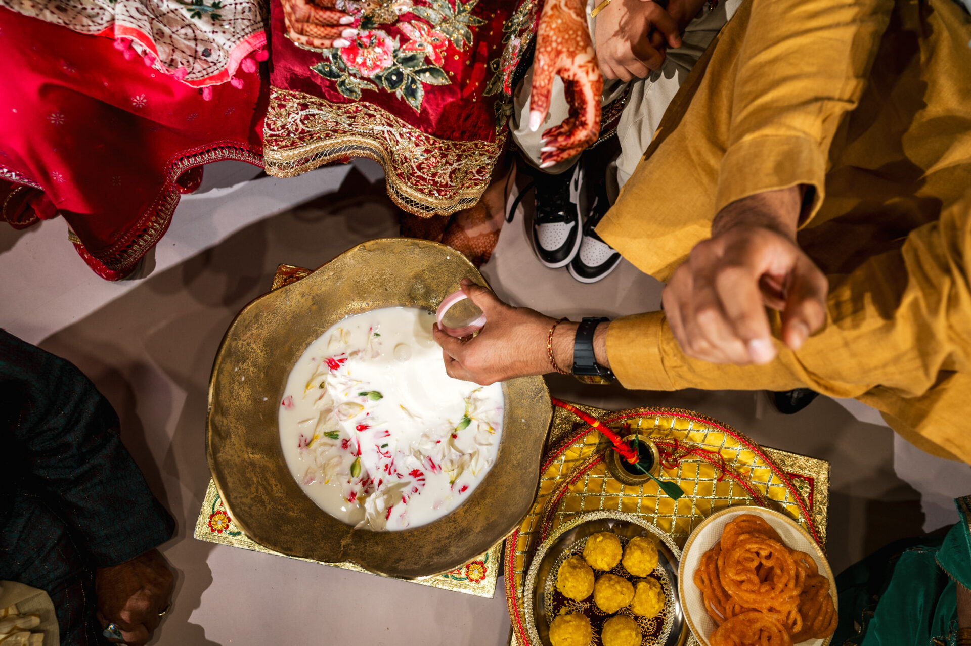 Top view of a Sikh ritual with milk, flowers, vibrant clothes, and sweets.