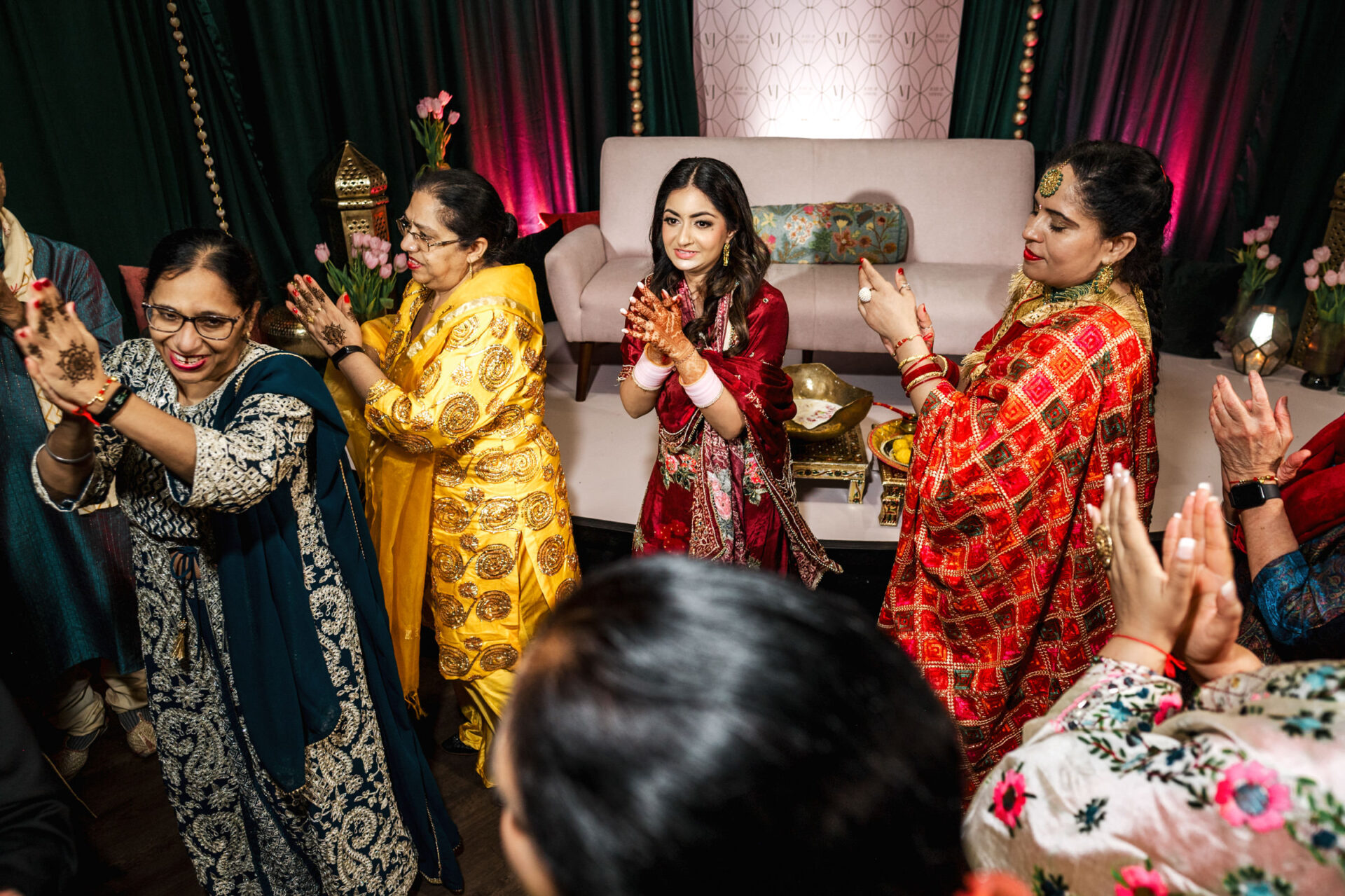 Women in colorful attire clapping and smiling at a vibrant Sikh wedding.