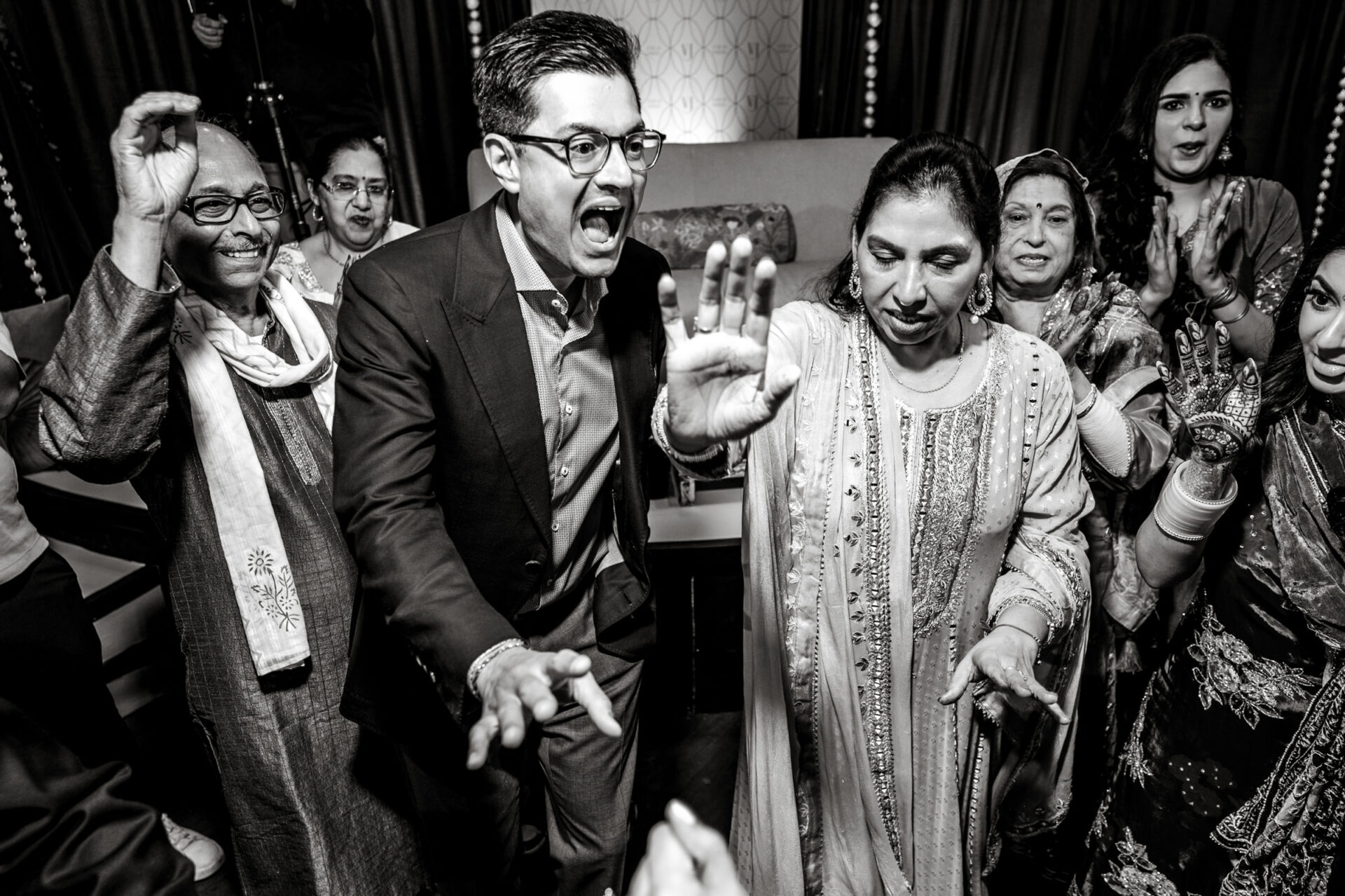 People dancing energetically at a lively Sikh wedding in formal and traditional attire.
