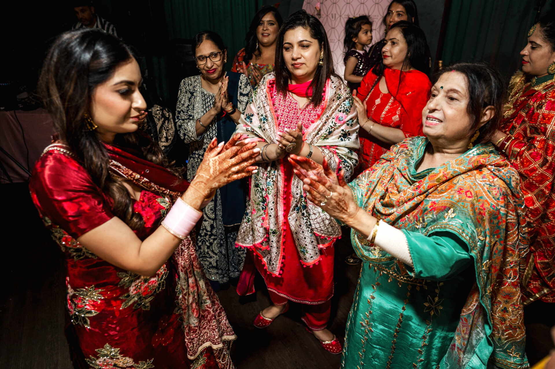 Women in colorful attire dancing at a vibrant Sikh wedding.