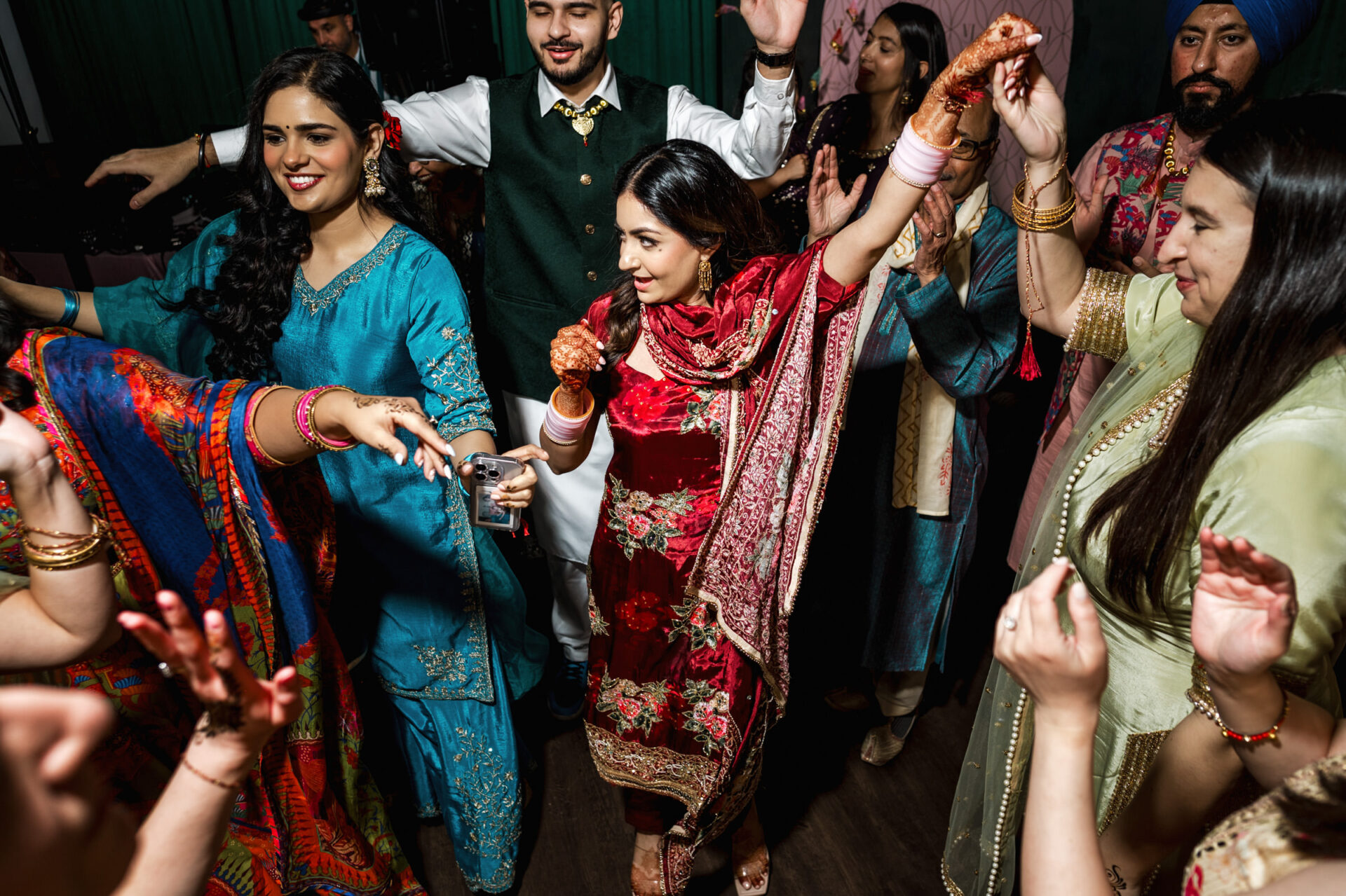Group dancing joyfully at a vibrant Sikh wedding in colorful traditional attire.