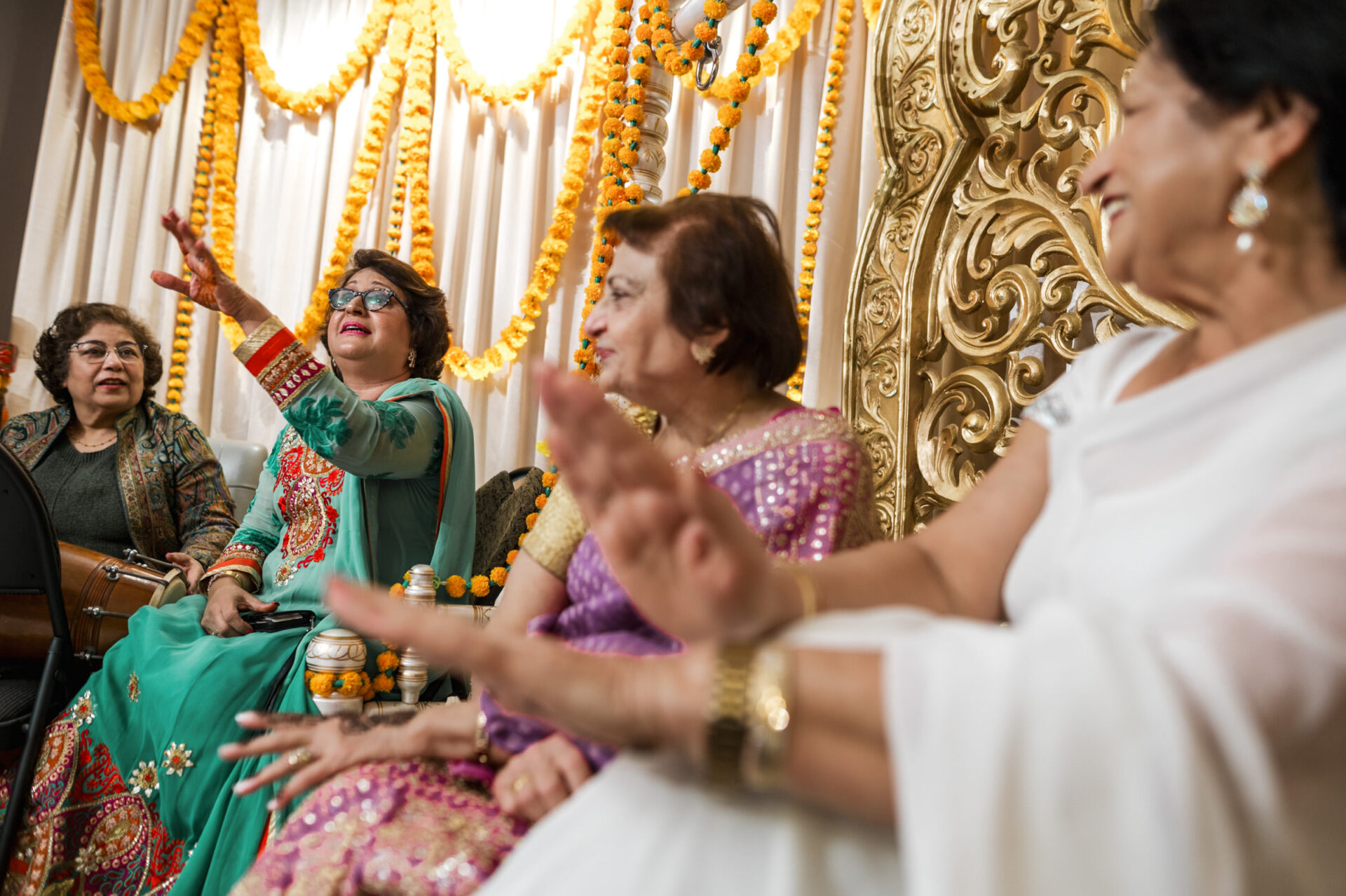 Group of women smiling and raising hands at a festive Sikh wedding event.