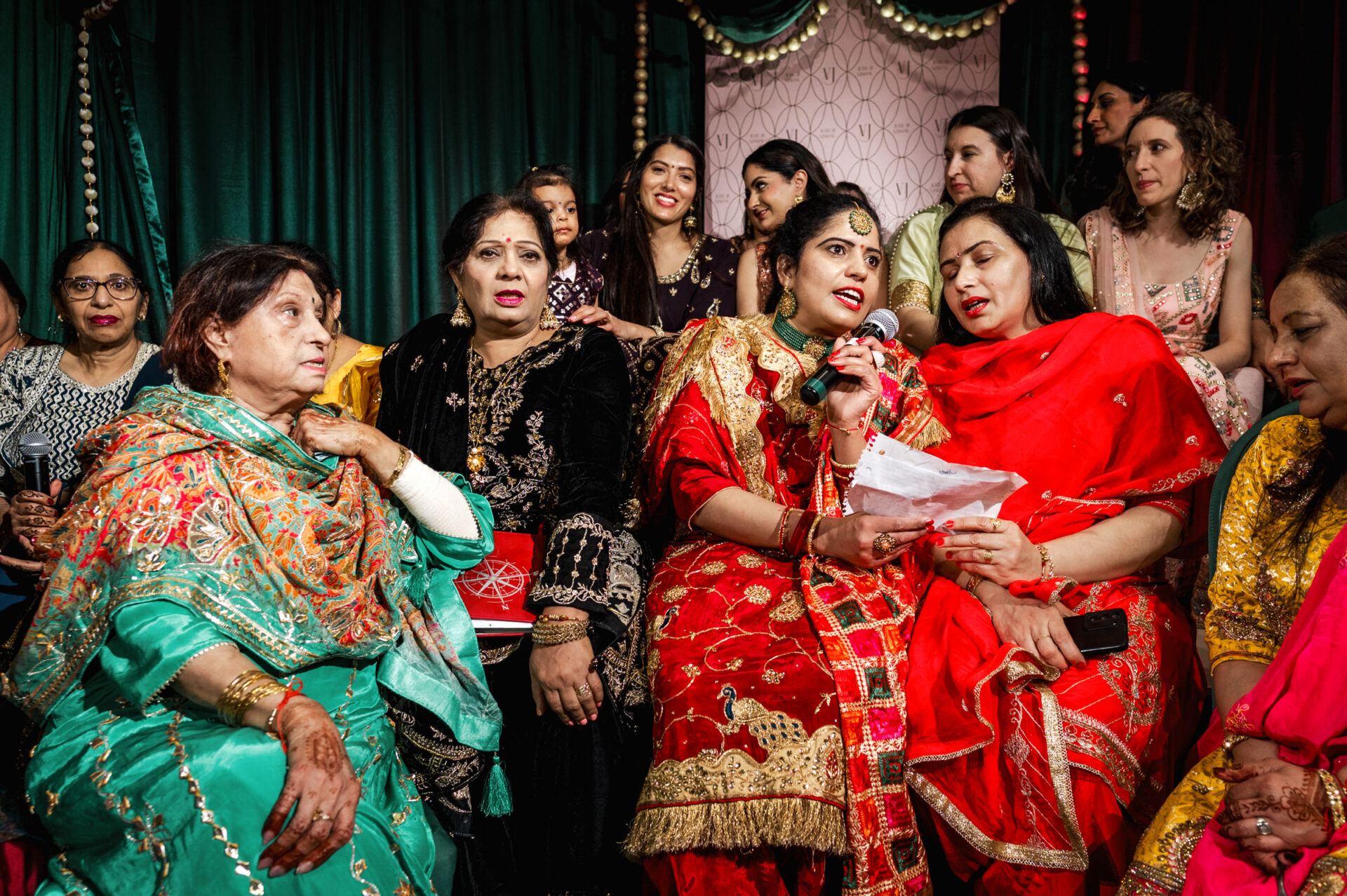 Women in colorful attire singing and celebrating at a lively Sikh wedding.