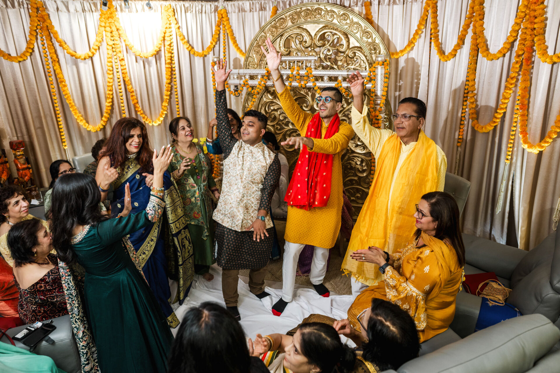 Sikh group celebrating in traditional attire, marigold garlands, ornate gold backdrop.