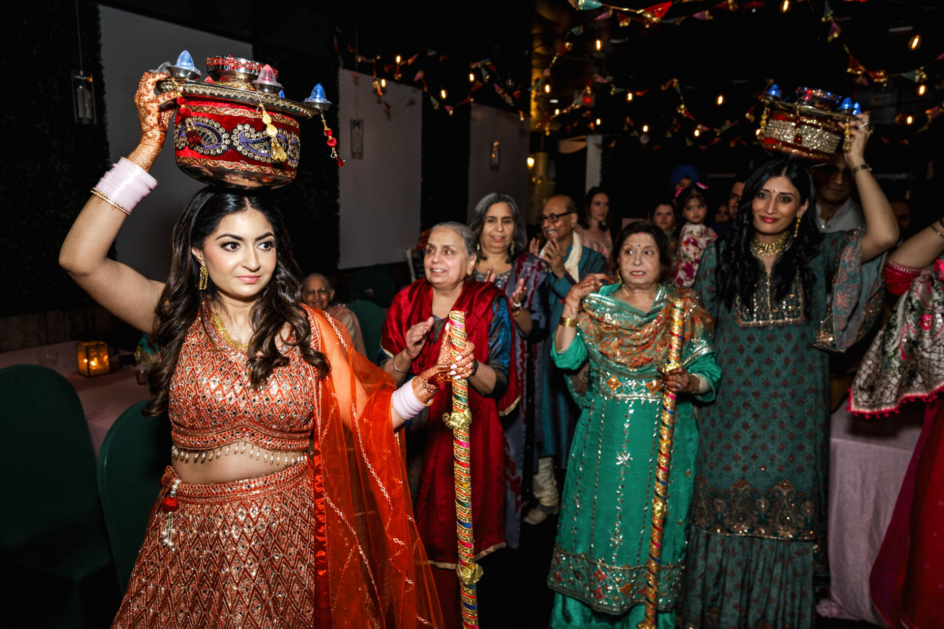 Women in colorful attire carrying pots at a lively Sikh wedding celebration.