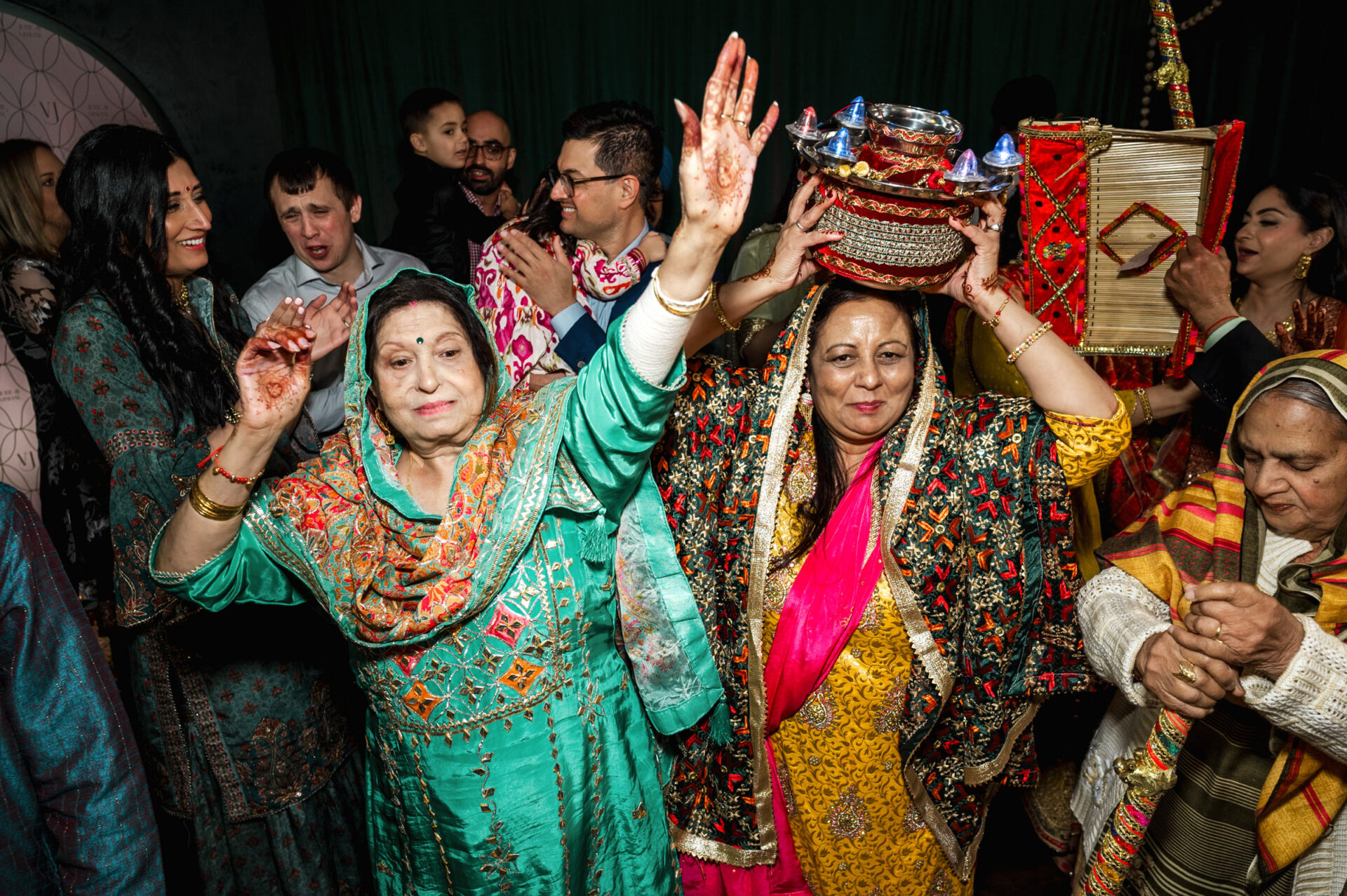 At a Sikh wedding, people dance as a woman balances a basket on her head.