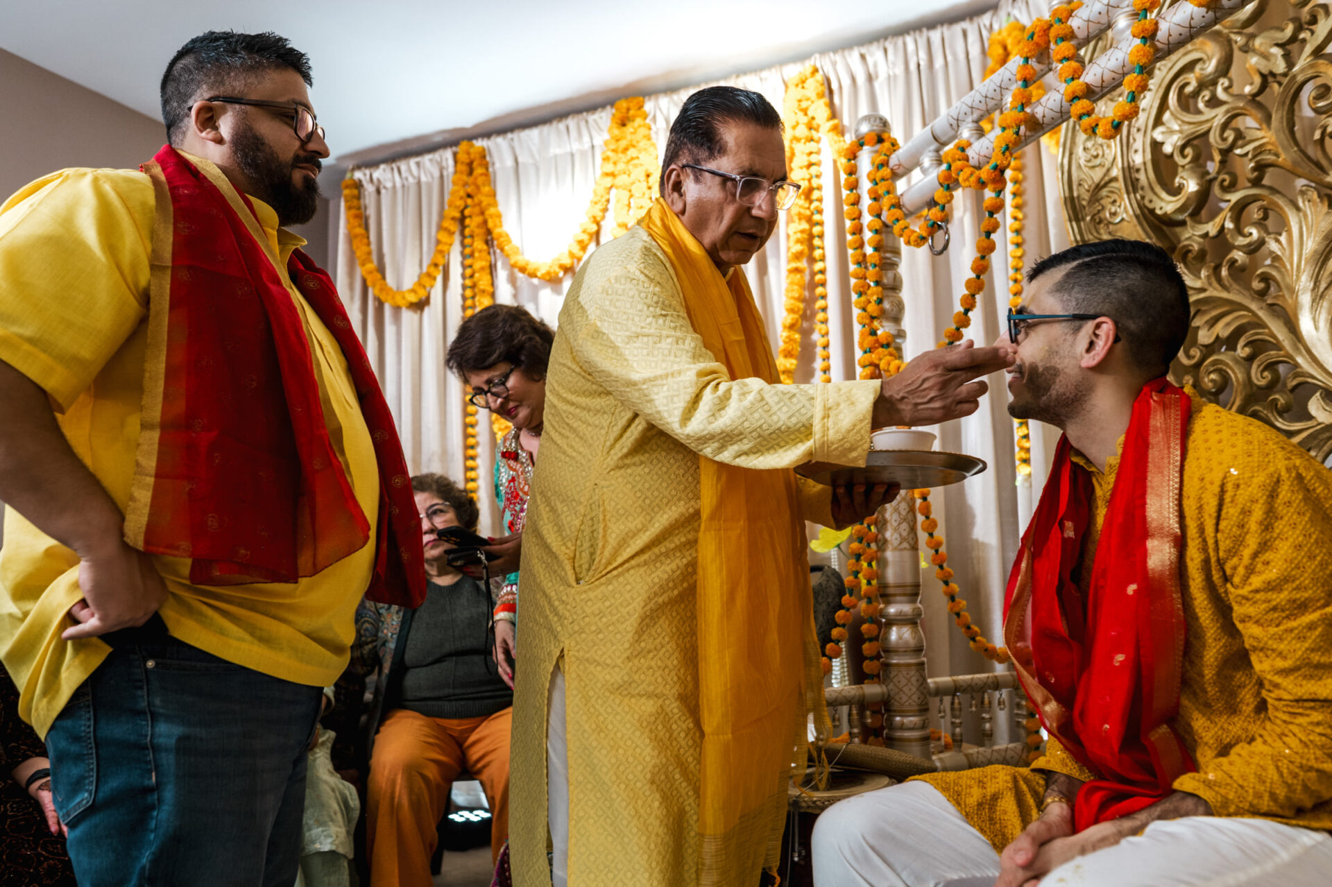 A traditional Sikh ceremony with yellow and red garments, floral décor in the background.