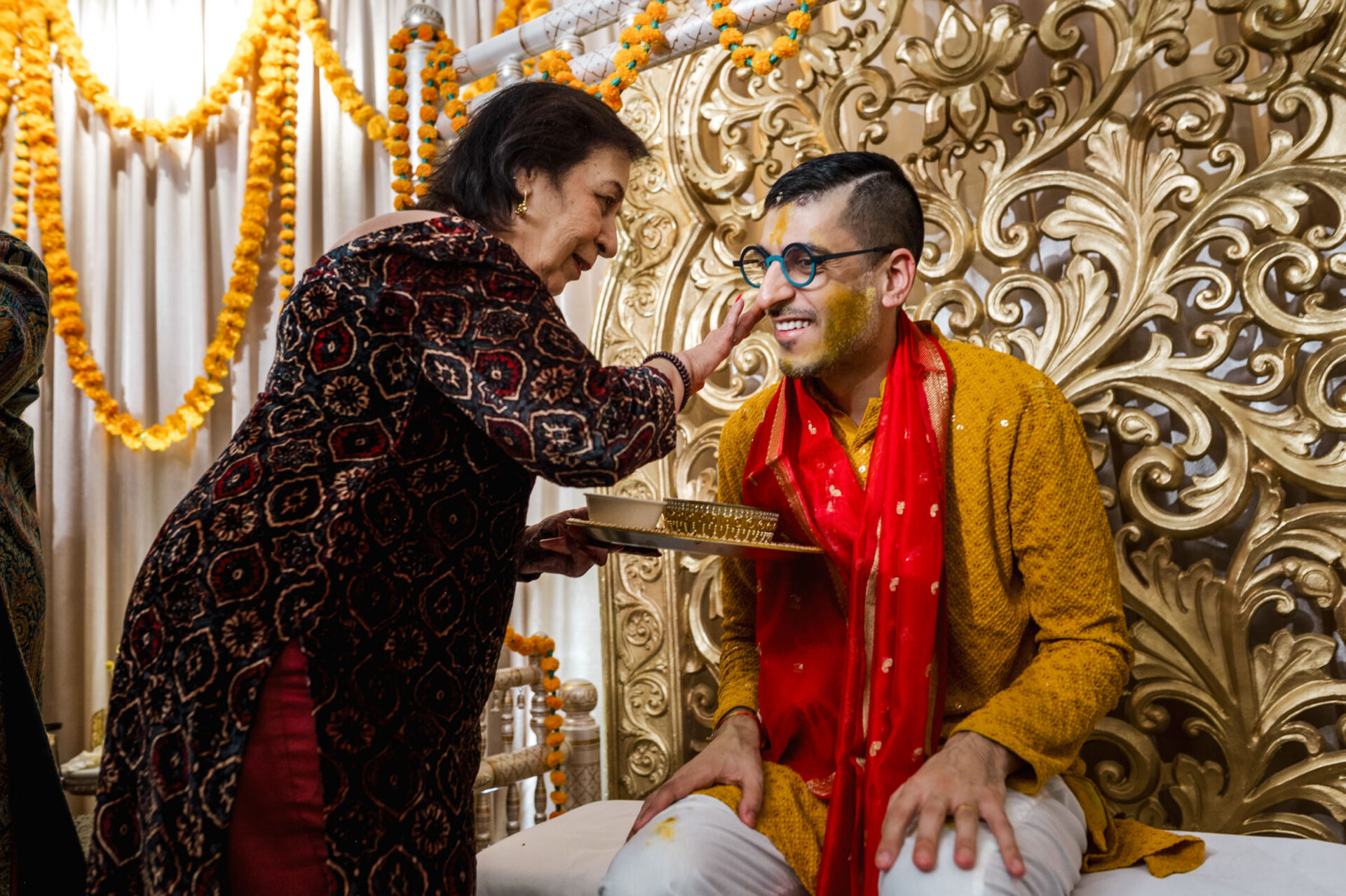 During a Sikh wedding, a woman applies turmeric to a smiling man in celebration.