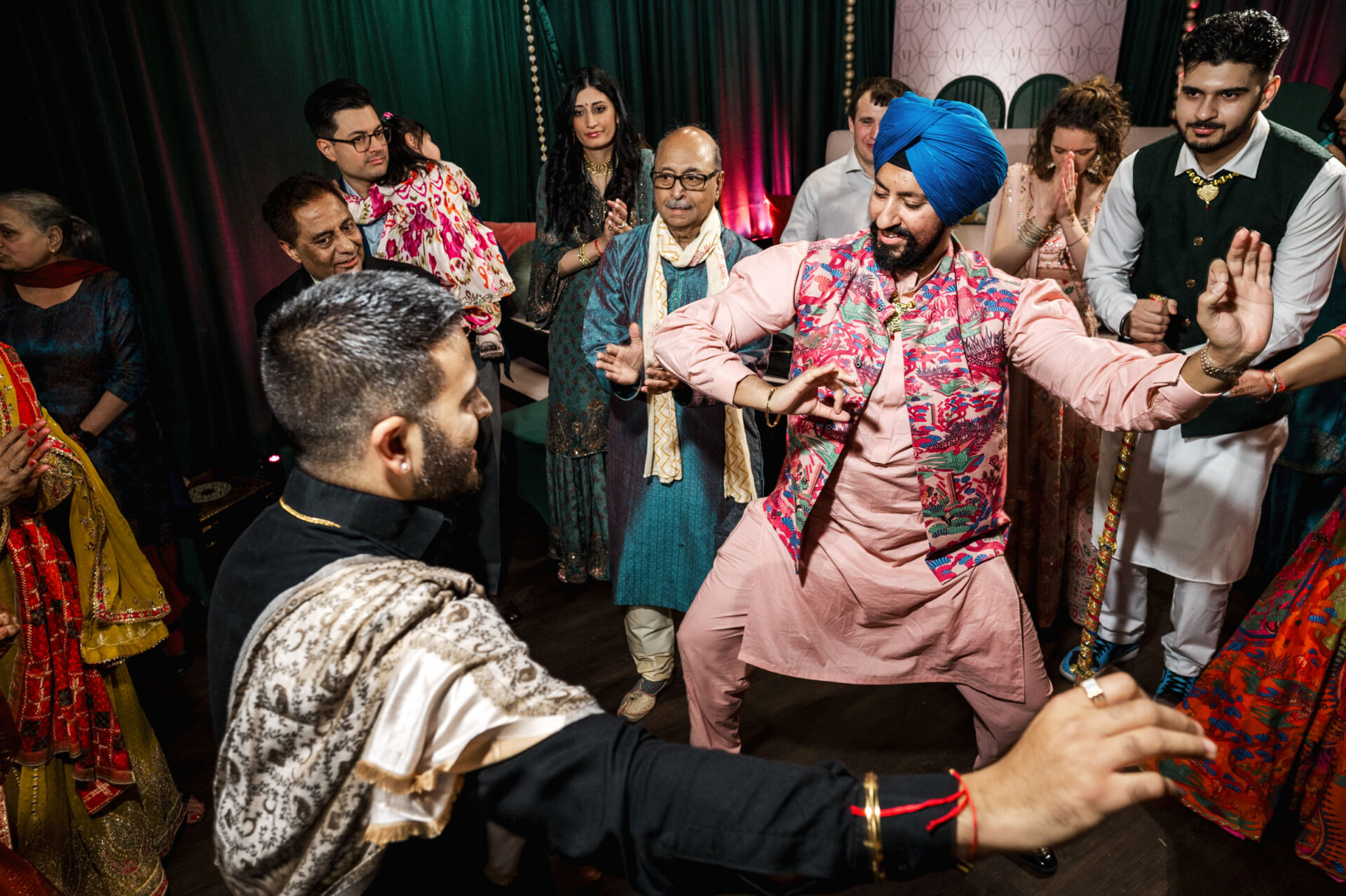 People in vibrant attire joyously dancing at a lively Sikh wedding celebration.