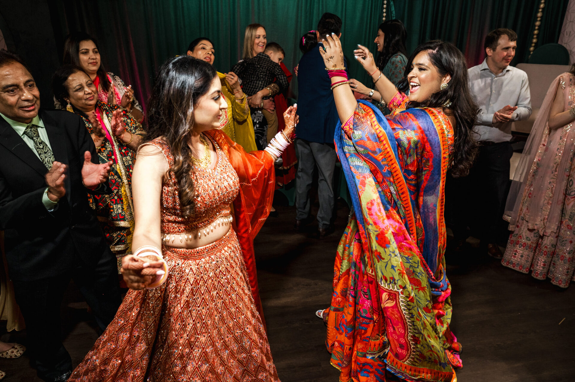 People dancing energetically at a Sikh wedding in colorful traditional clothing.