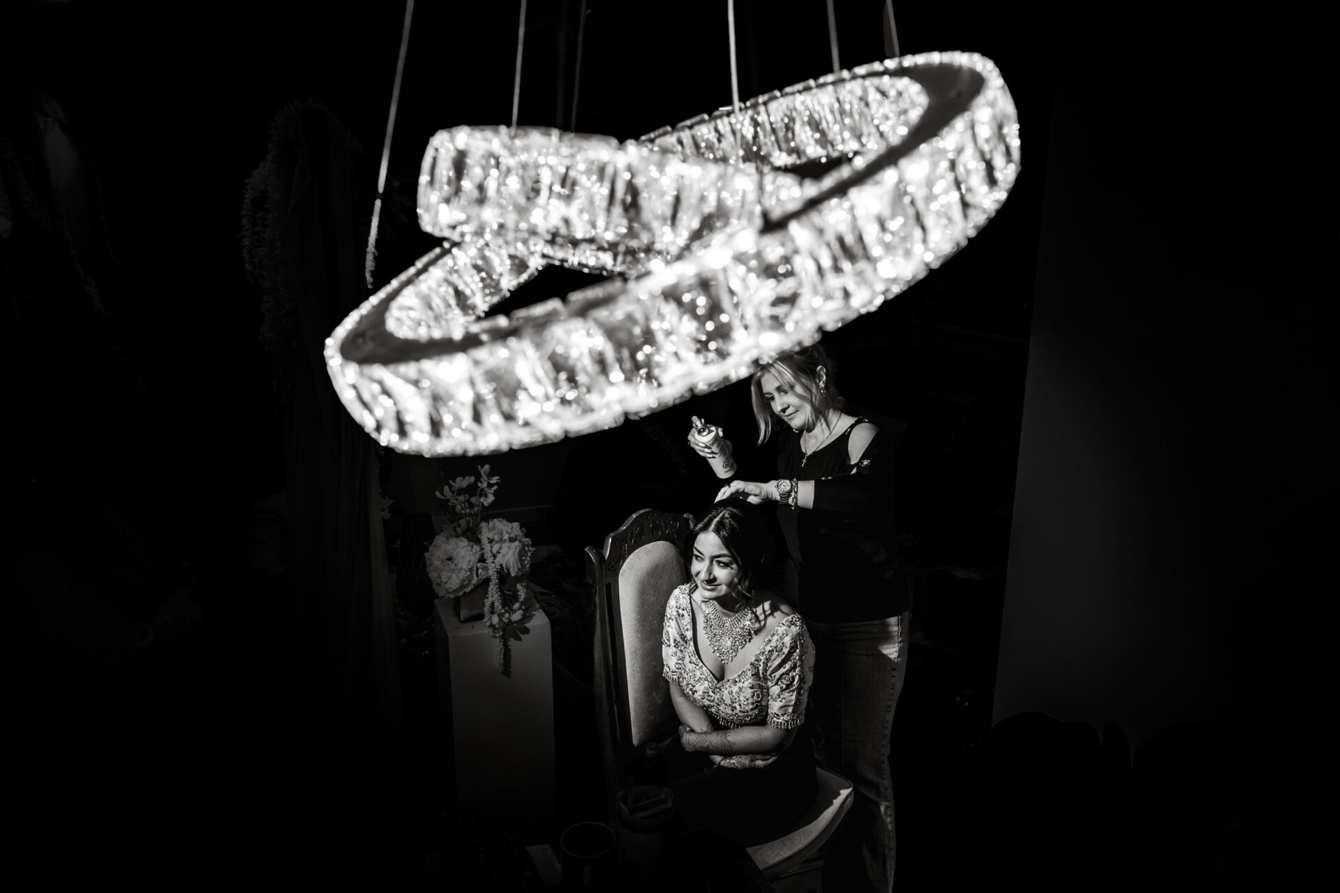 Woman styling another's hair under a chandelier at a Sikh wedding.