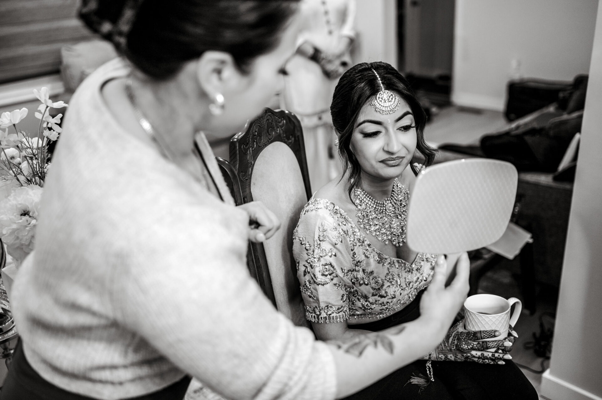 Bride checking her reflection in a hand mirror at a Sikh wedding, assisted by another woman.