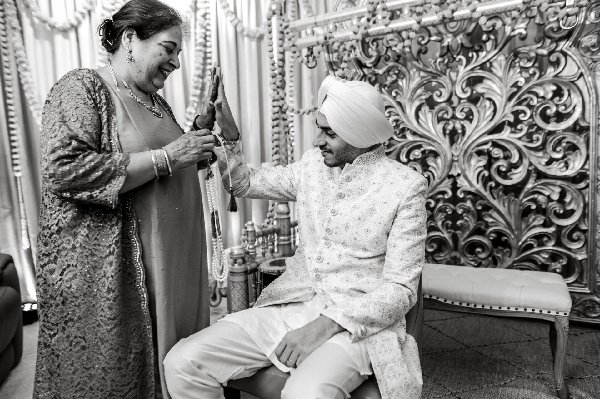 A joyful moment between a woman and a seated man in traditional attire at a Sikh wedding.