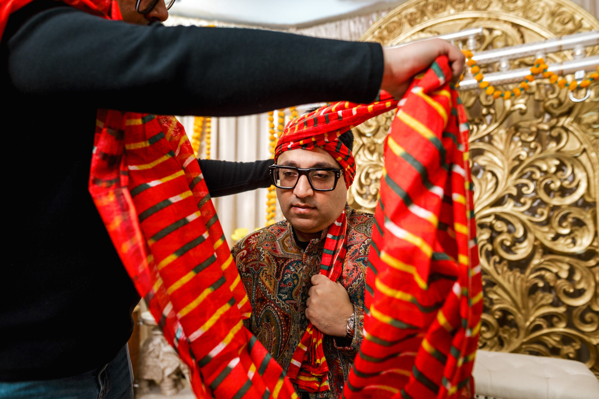 Sikh man in colorful turban, adjusted against ornate gold wedding backdrop.