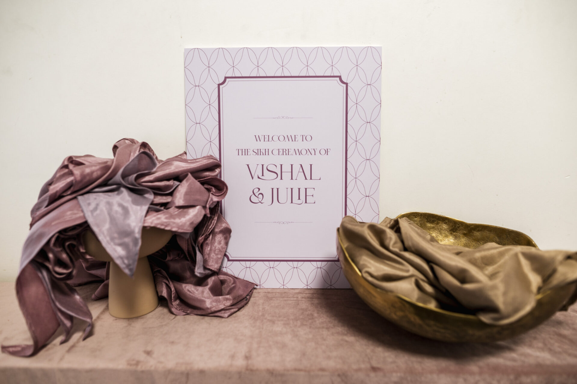 Silk fabrics and a sign for Vishal & Jule's Sikh & Hindu wedding on a table.