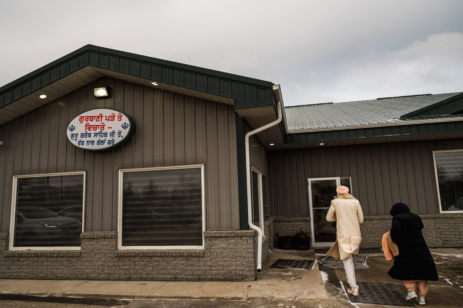 Two people entering a building with a sign, like at a Sikh or Hindu wedding.