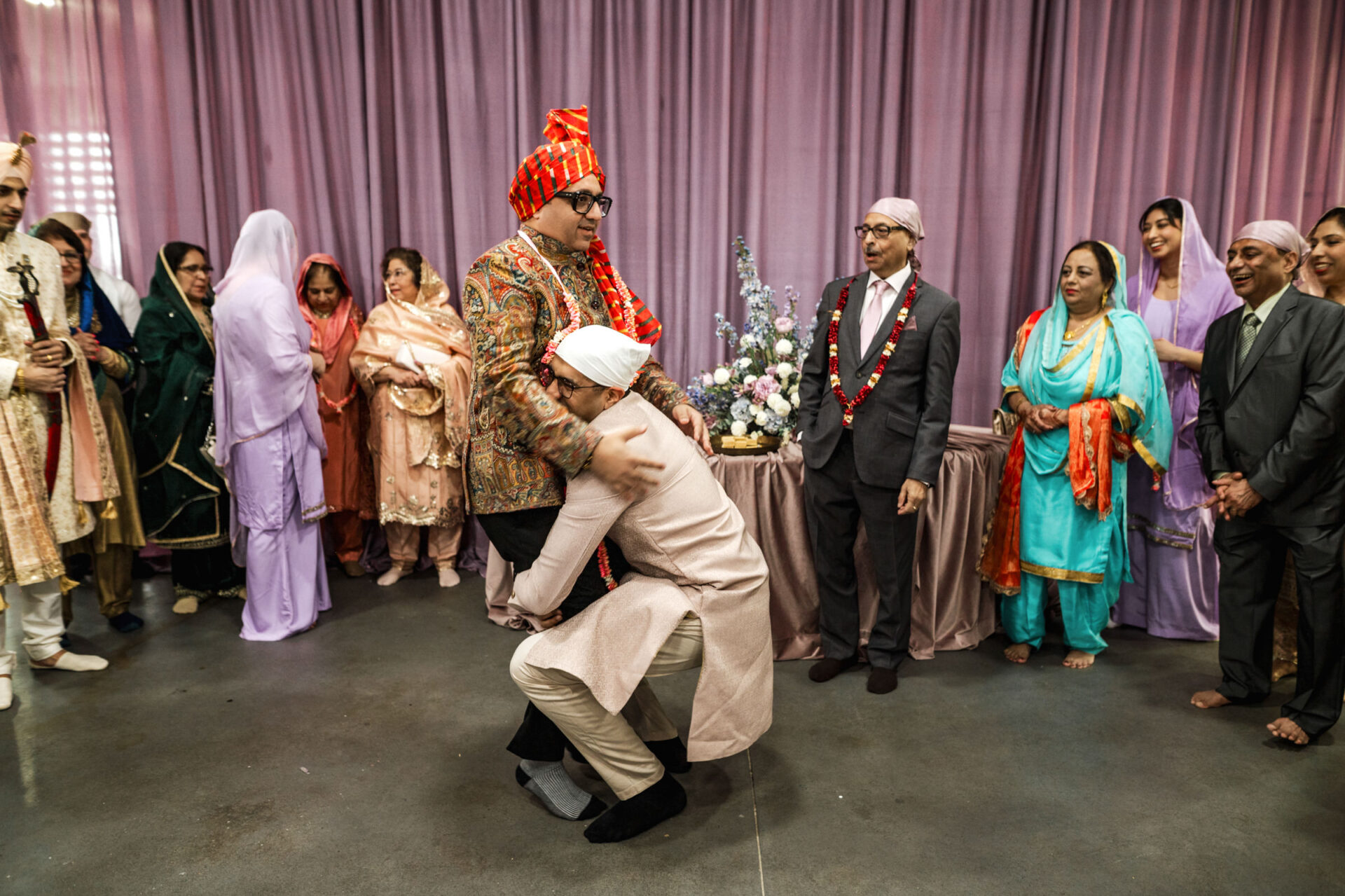 Group at a Sikh wedding; one hugs another's legs, others watch with smiles.