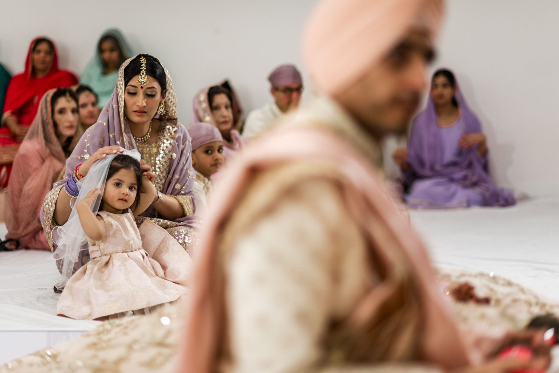 Child in traditional attire with adults at a Sikh wedding ceremony.