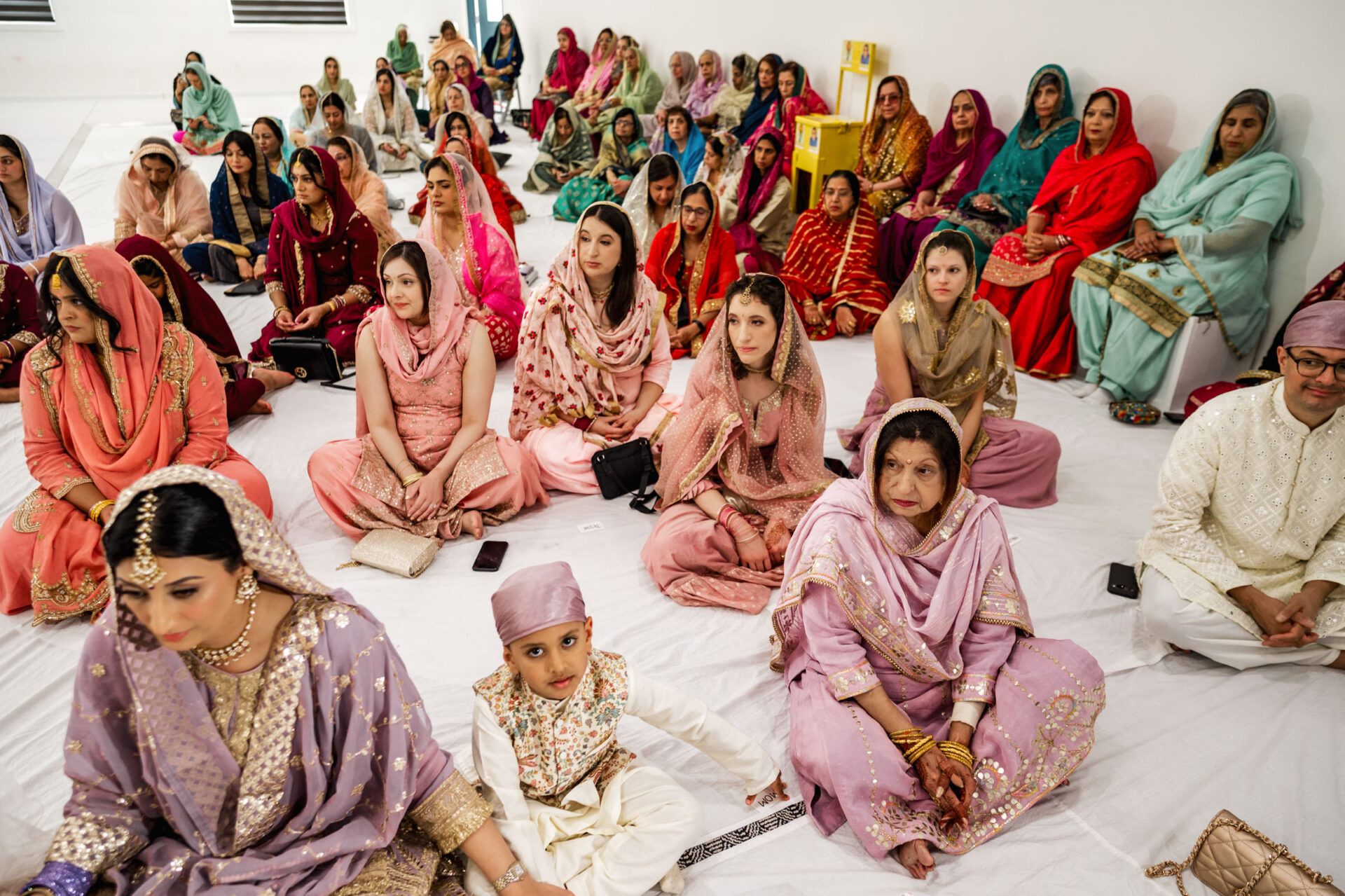 A diverse group seated on the floor in traditional attire at a Sikh wedding gathering.
