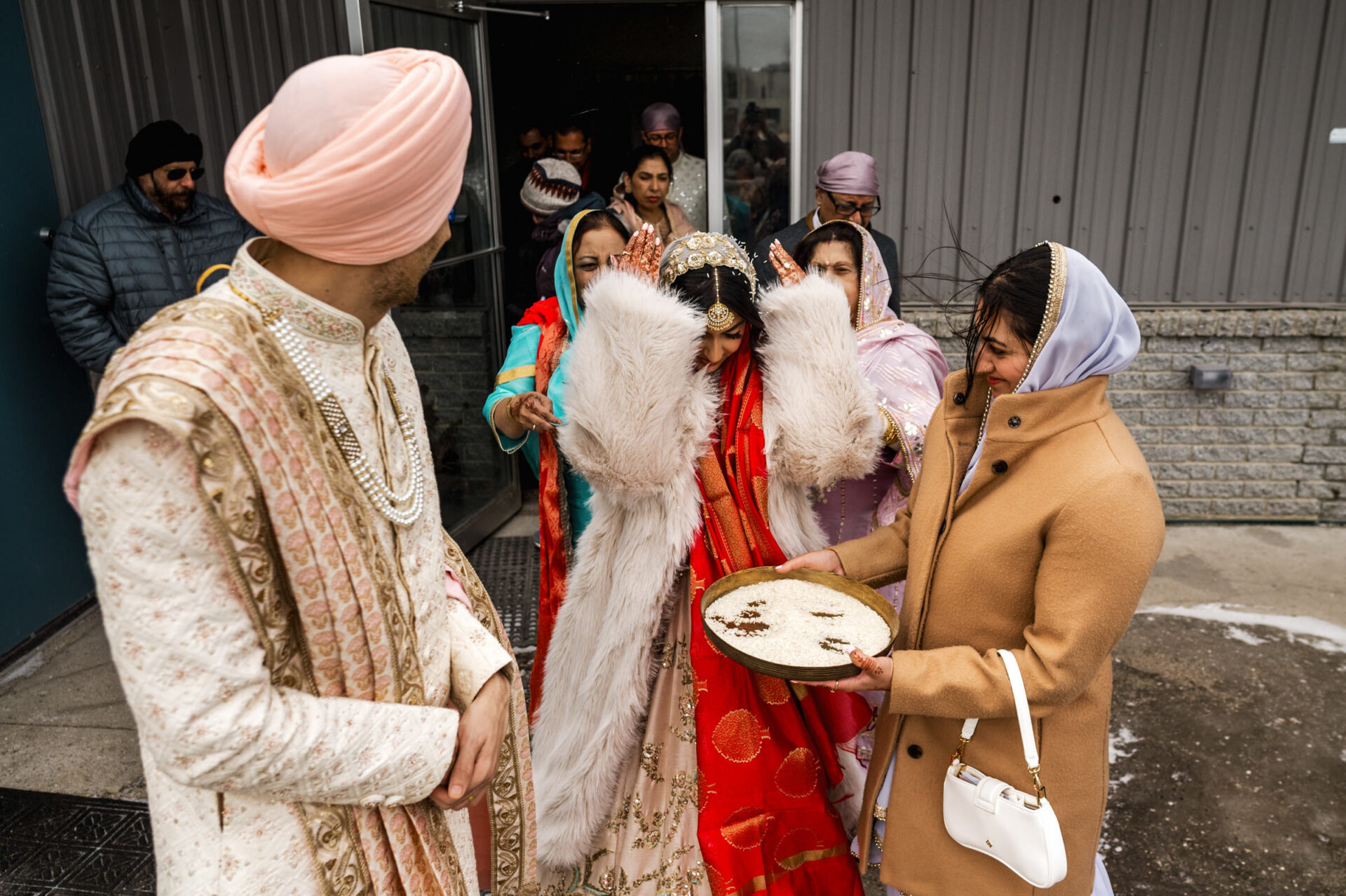 A bride and groom exit during a Sikh wedding, surrounded by joyful family.