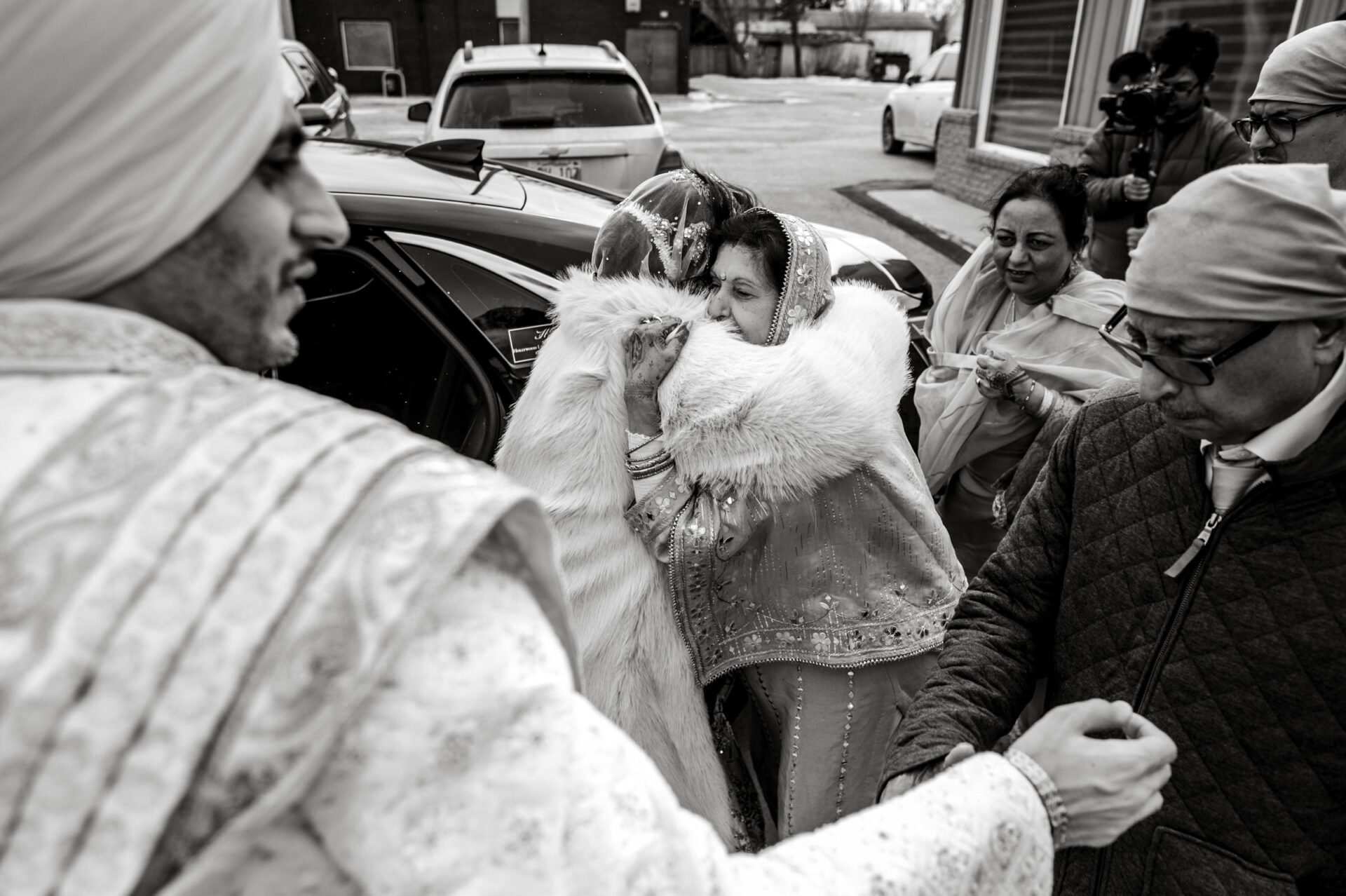 A woman in traditional attire hugs a man at a Sikh wedding, surrounded by snow and guests.