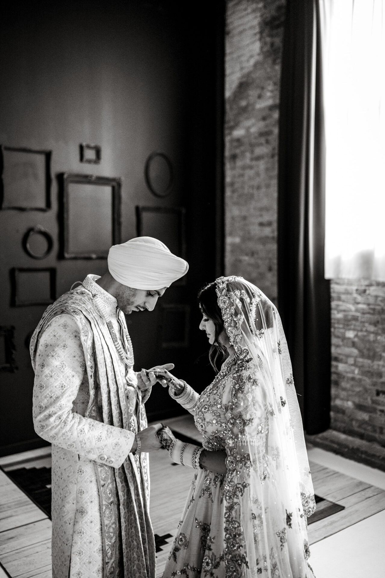A bride and groom in traditional attire share a moment at their Sikh wedding indoors.