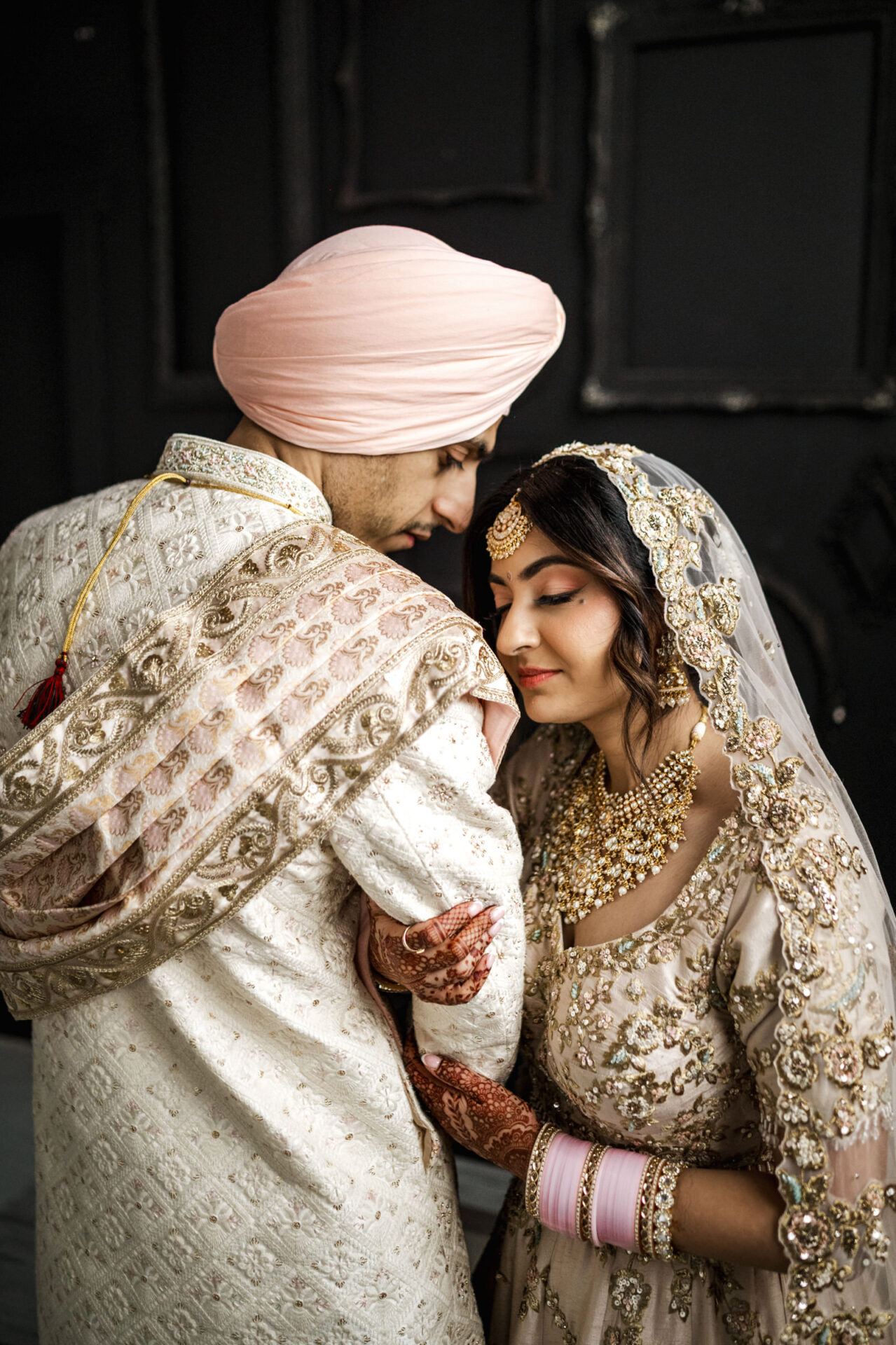A bride and groom, in traditional Sikh attire, share an intimate moment.