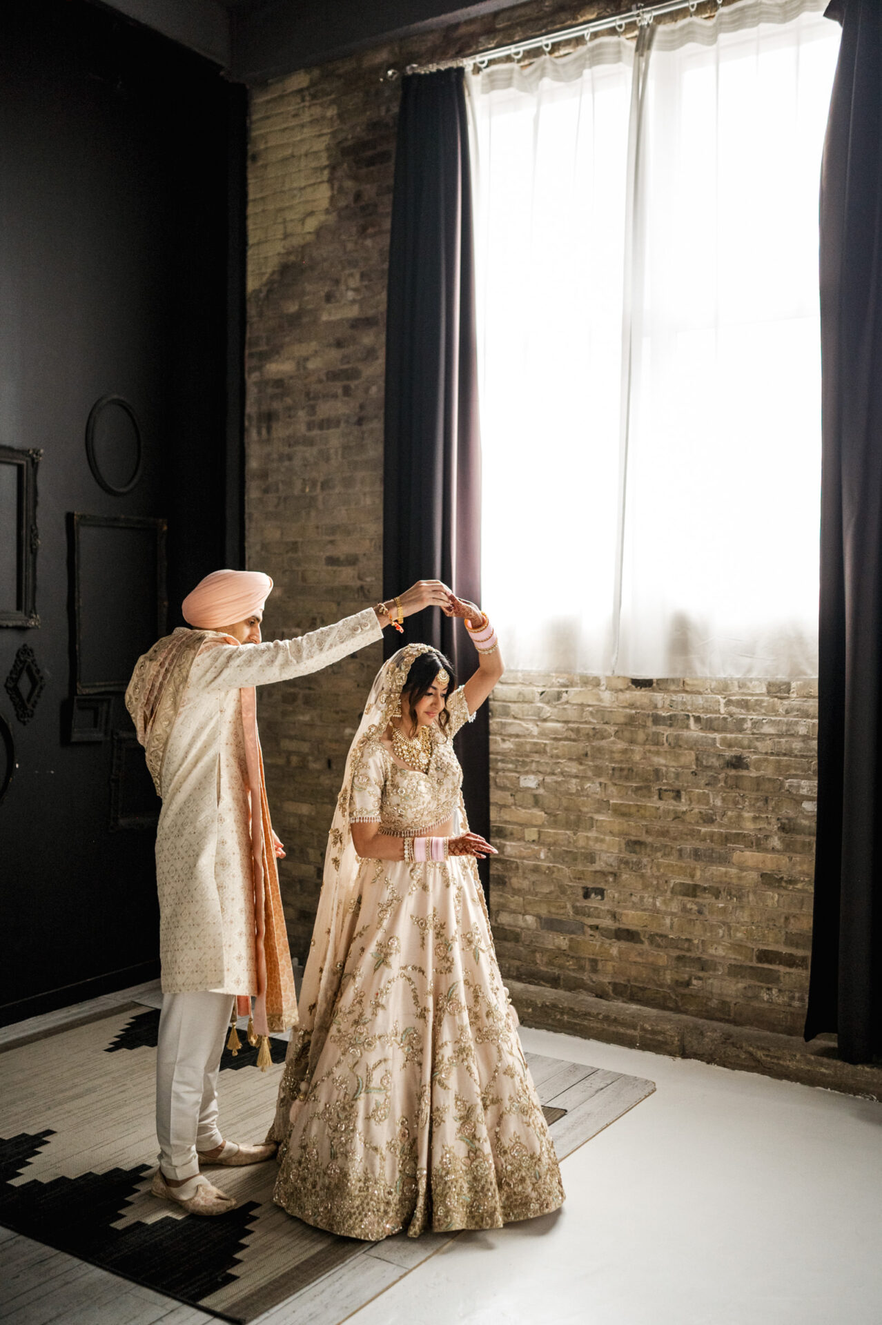 A couple dances in traditional attire by a window, celebrating a Sikh wedding.