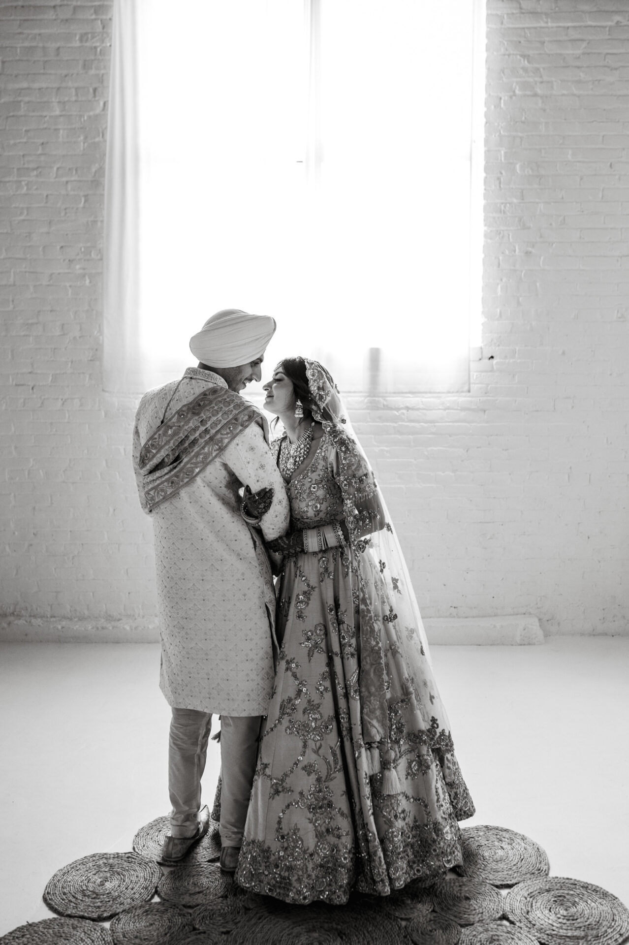 Couple in Sikh attire sharing an intimate moment by a sunlit window.