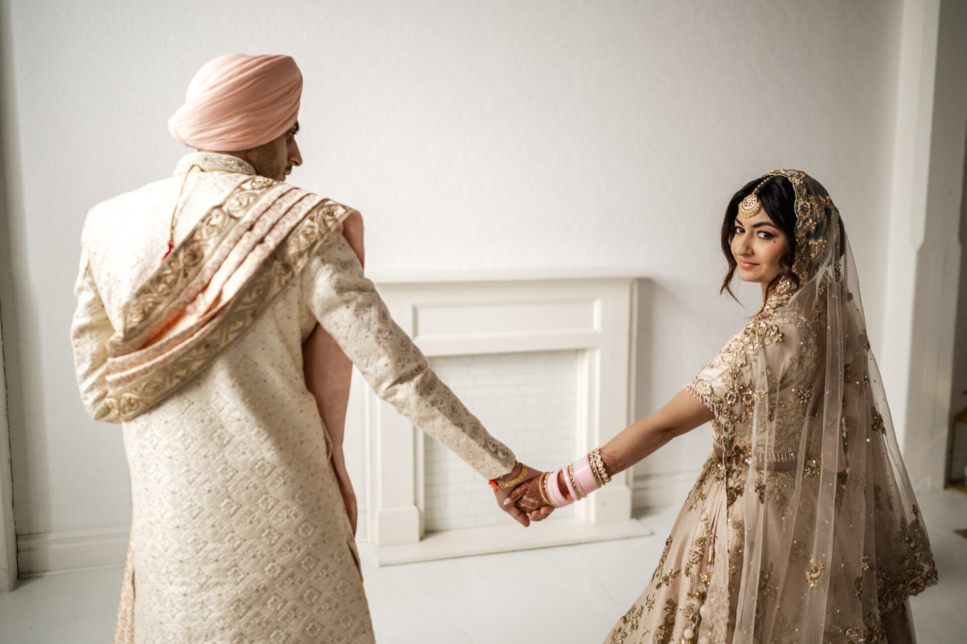 Bride and groom in traditional attire at a Sikh wedding, holding hands and gazing at each other.