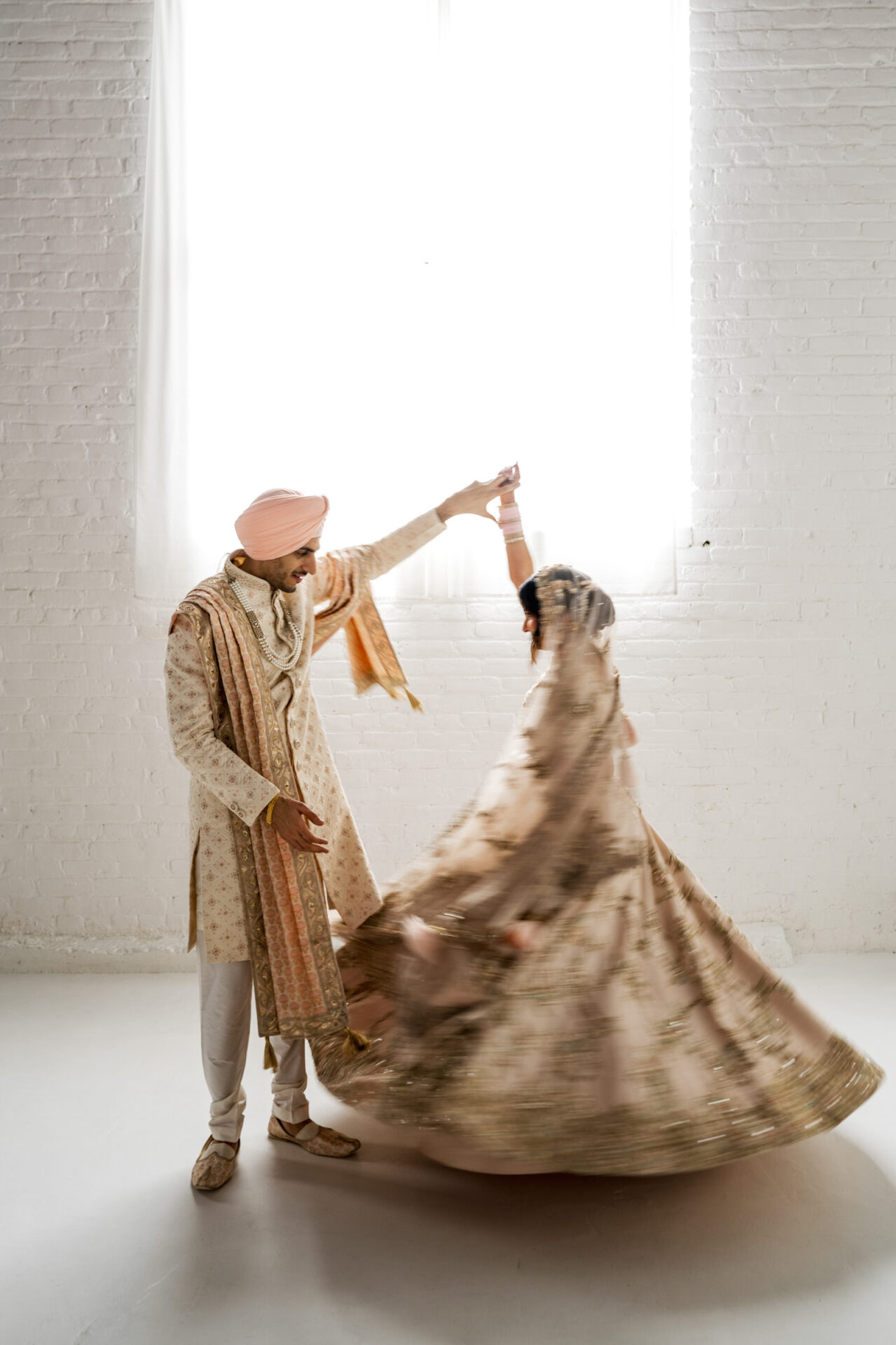 Couple in traditional attire dancing at a softly lit Sikh wedding.