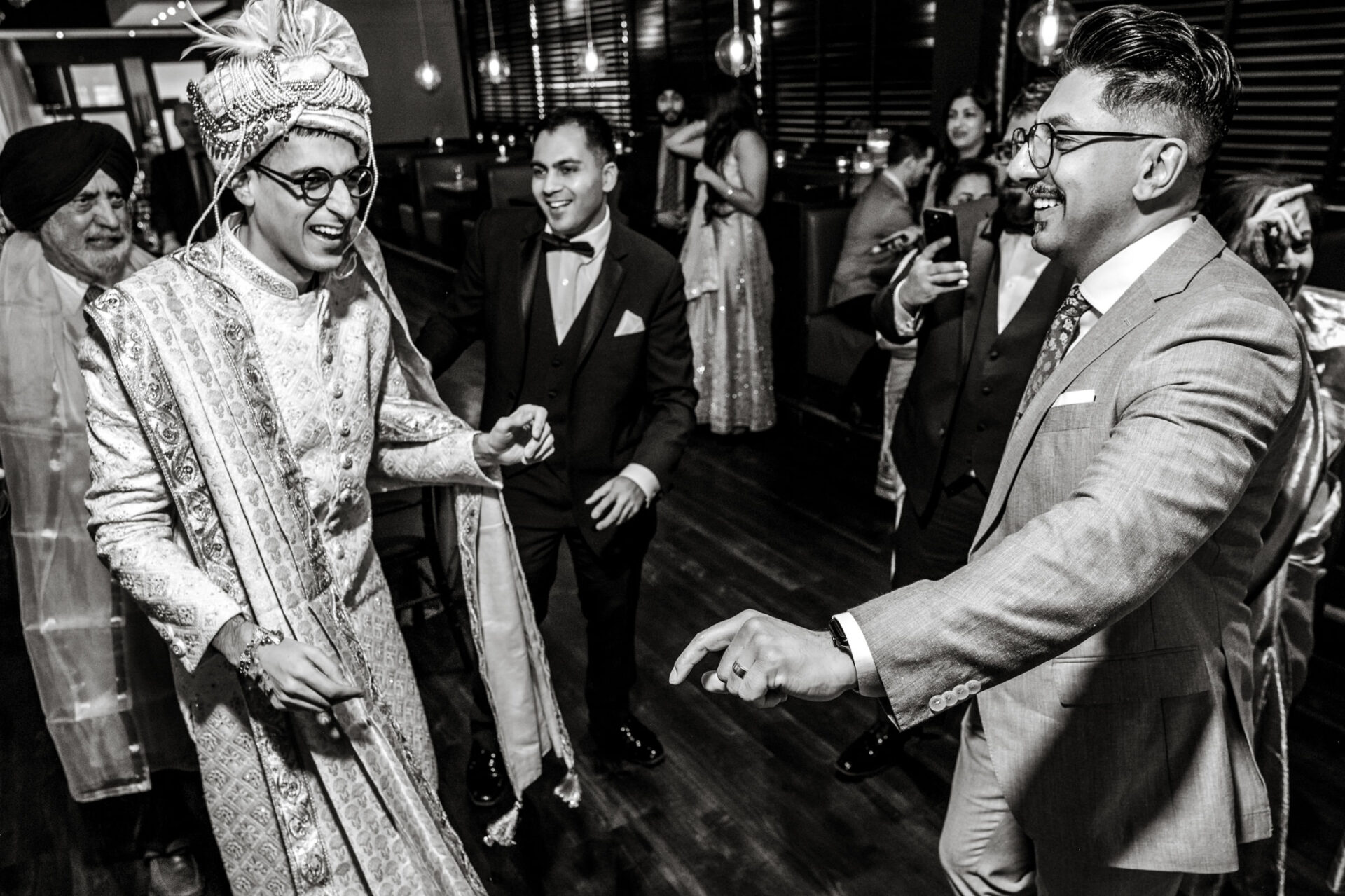 Groom in traditional attire joyfully dances with friends at a Sikh celebration.