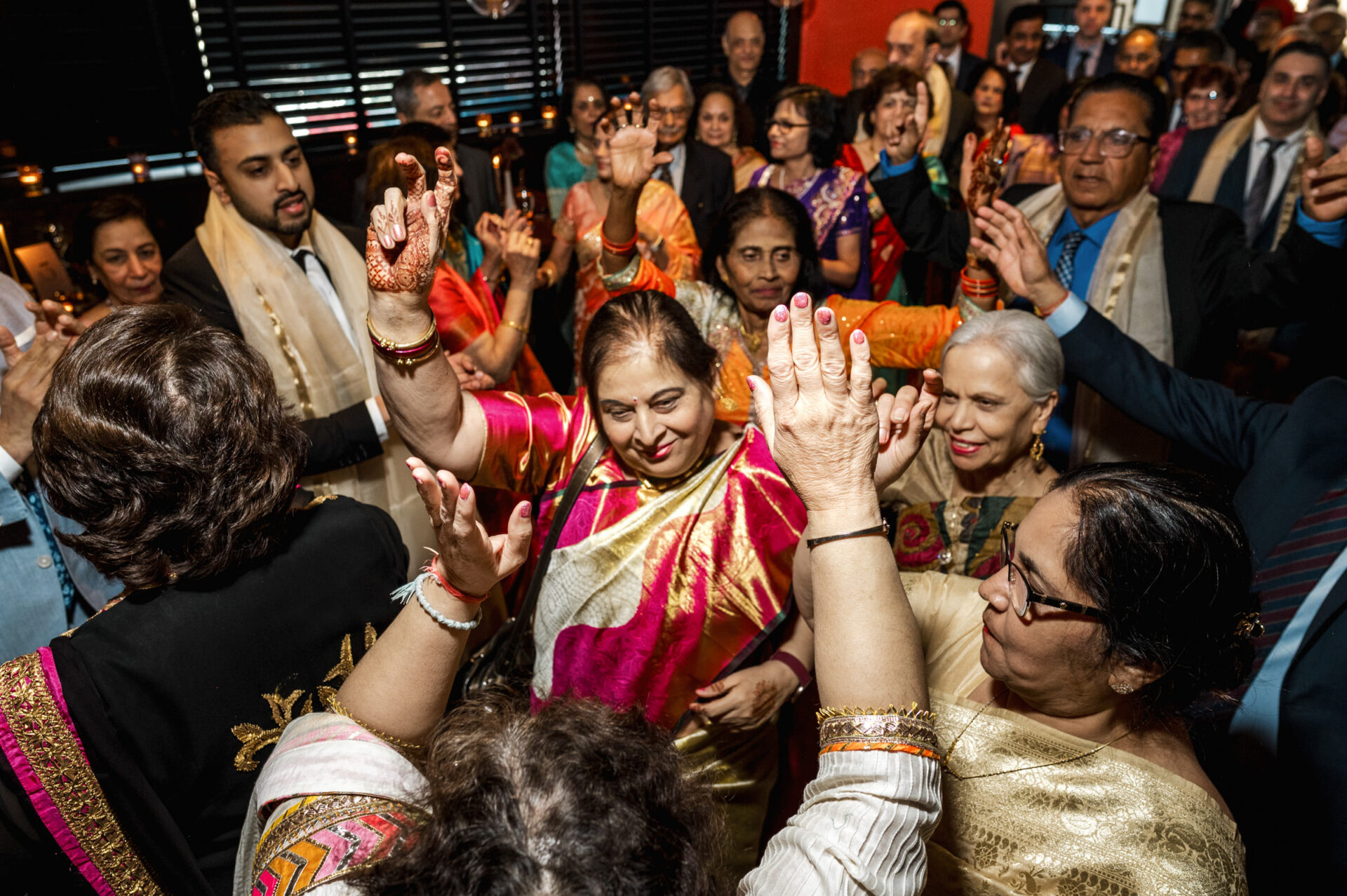 People joyfully dancing in colorful attire at a festive Sikh wedding gathering.