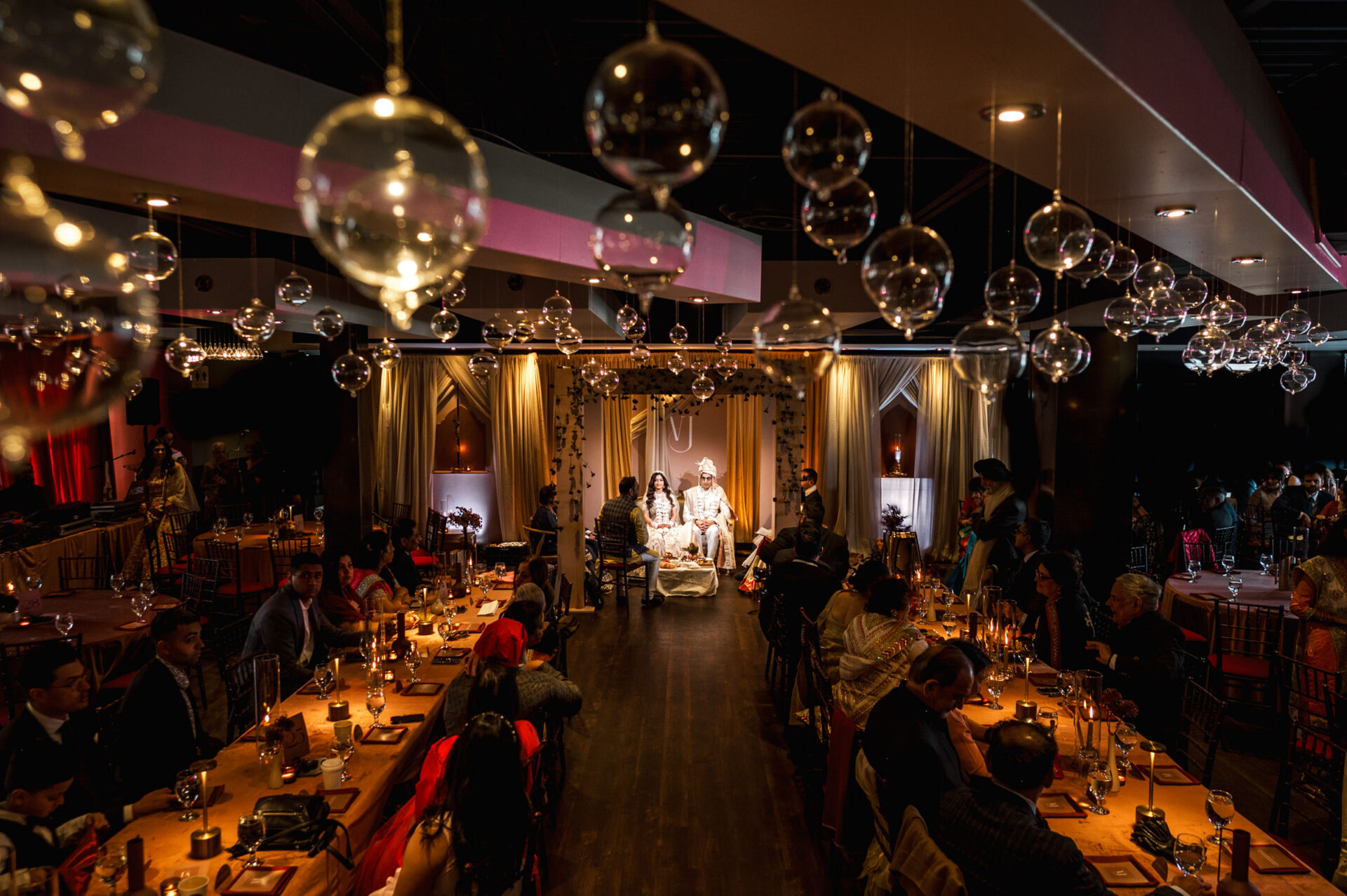 Sikh wedding in a dim venue with glass orbs and seated guests.